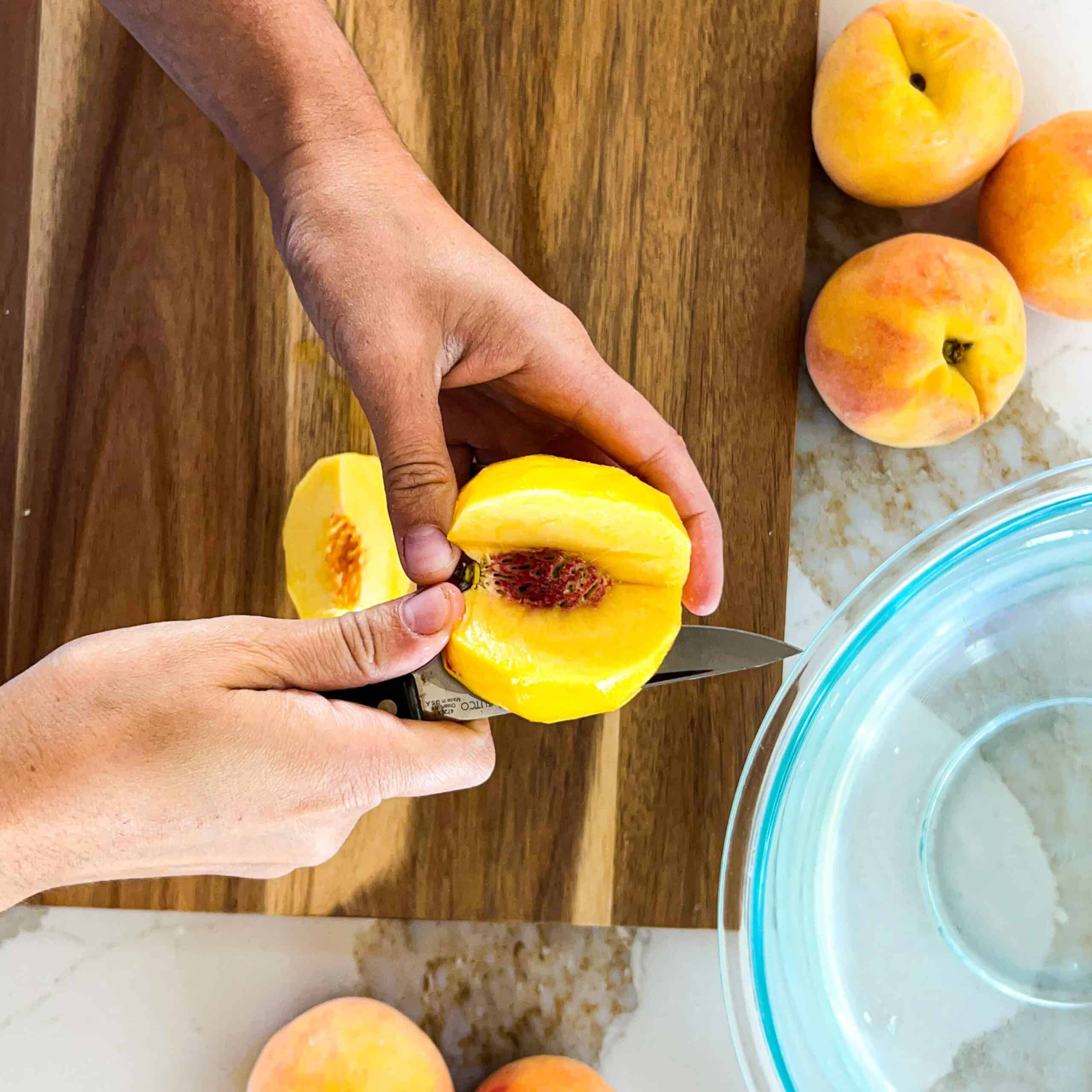 A peeled peach being cut off of the pit in slices.