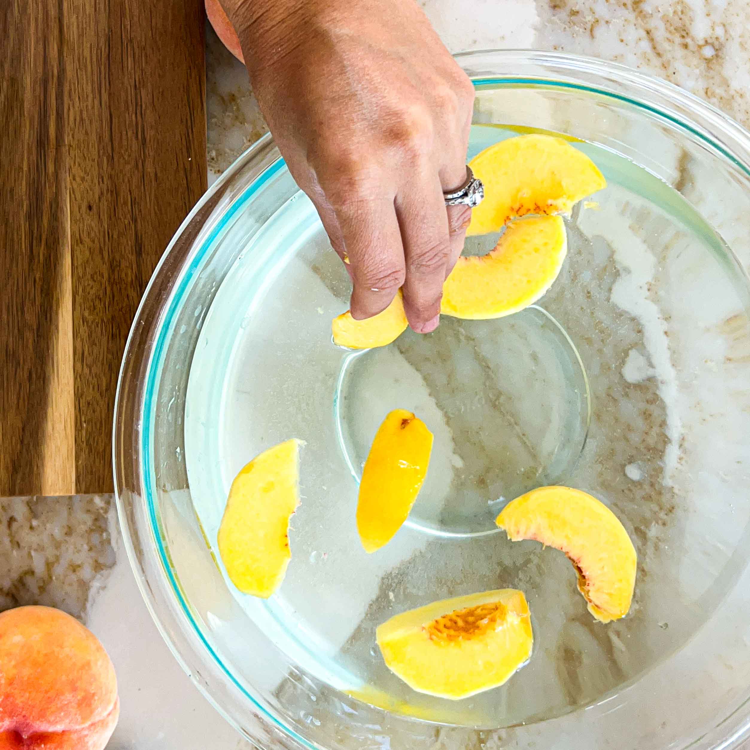 Fresh peach slices soaking in a bowl of lemon water.