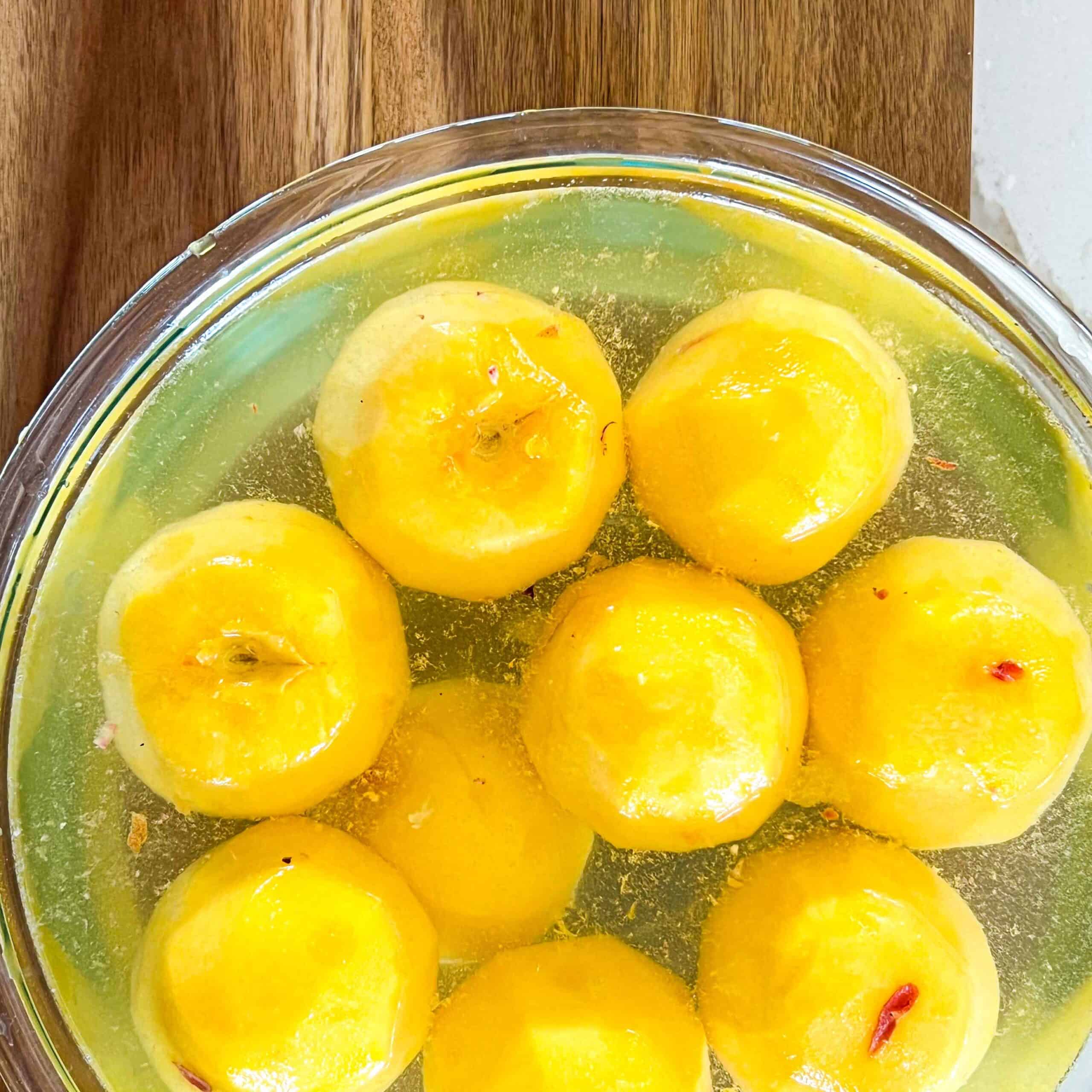 Peeled peaches in a large glass bowl with a lemon and water solution to keep them fresh.