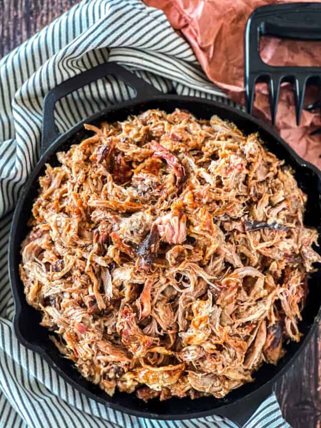 Traeger pulled pork in a cast iron pan with a striped linen napkin wrapped halfway around and meat claws.