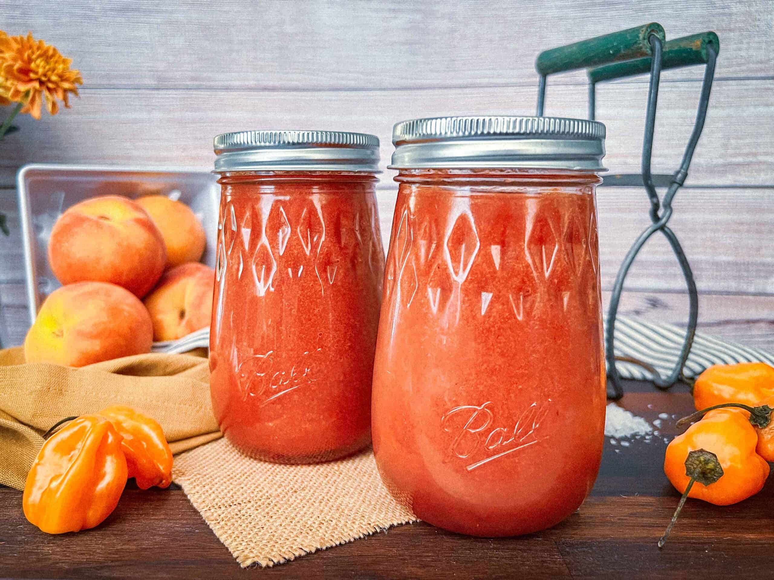 Smoked peach habanero hot sauce in jars with salt, peppers, peaches on a wooden cutting board.