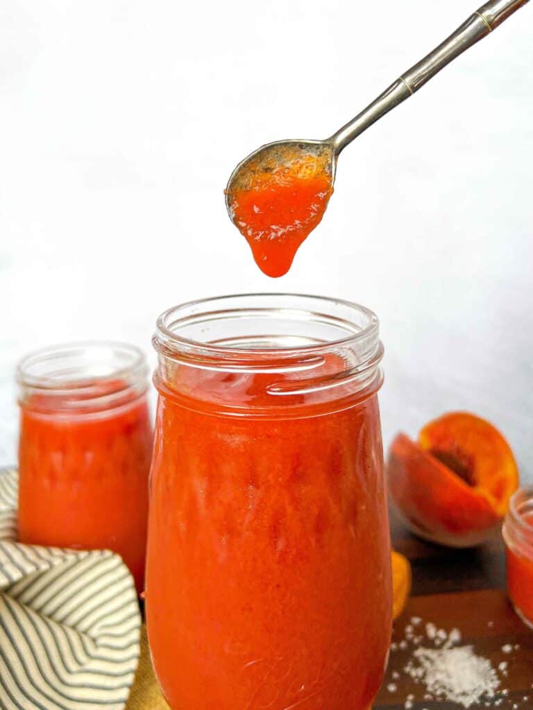 Smoked peach habanero hot sauce dripping into a pint jar off of an antique silver spoon.
