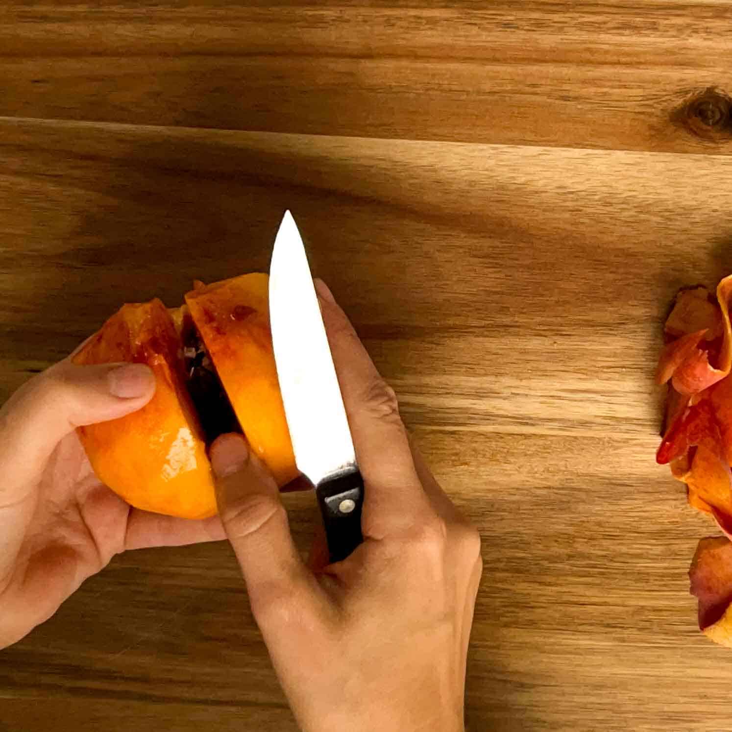 Slicing a peach in half overtop of a wooden cutting board.