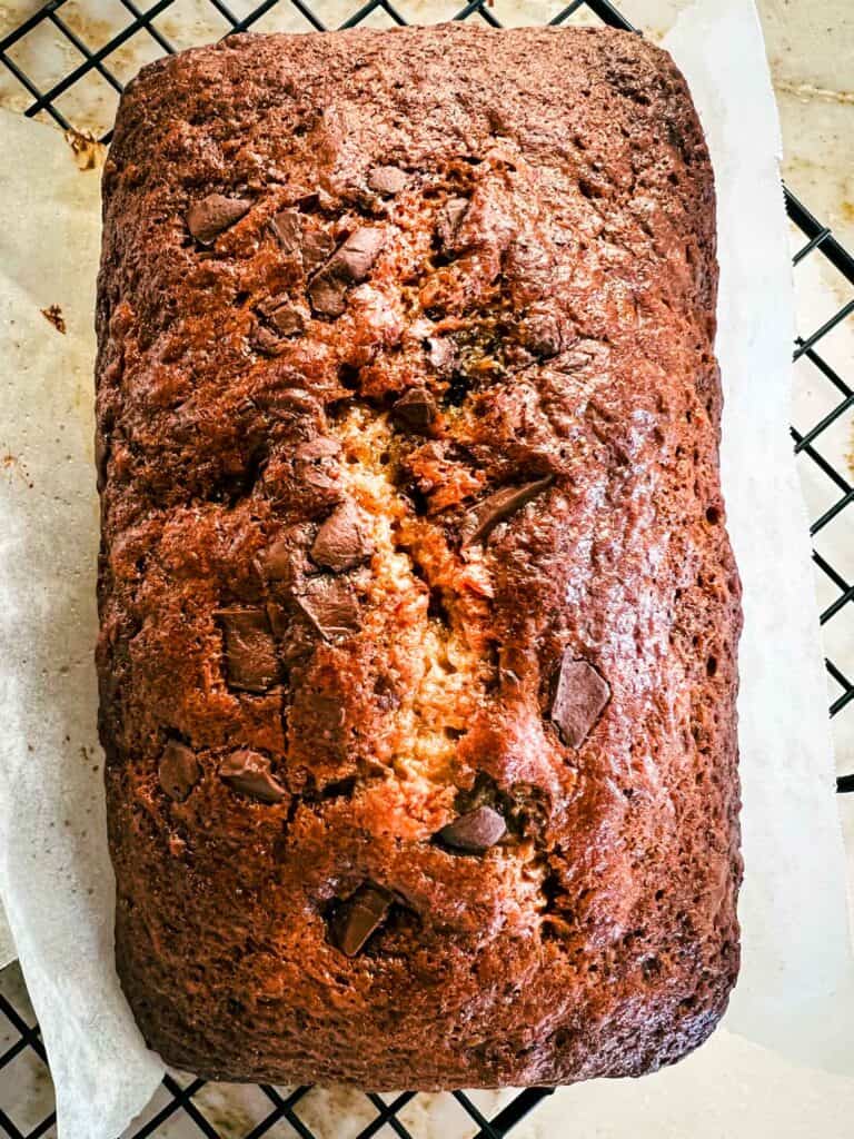 Banana bread without butter baked and sitting on a piece of parchment and cooling rack.