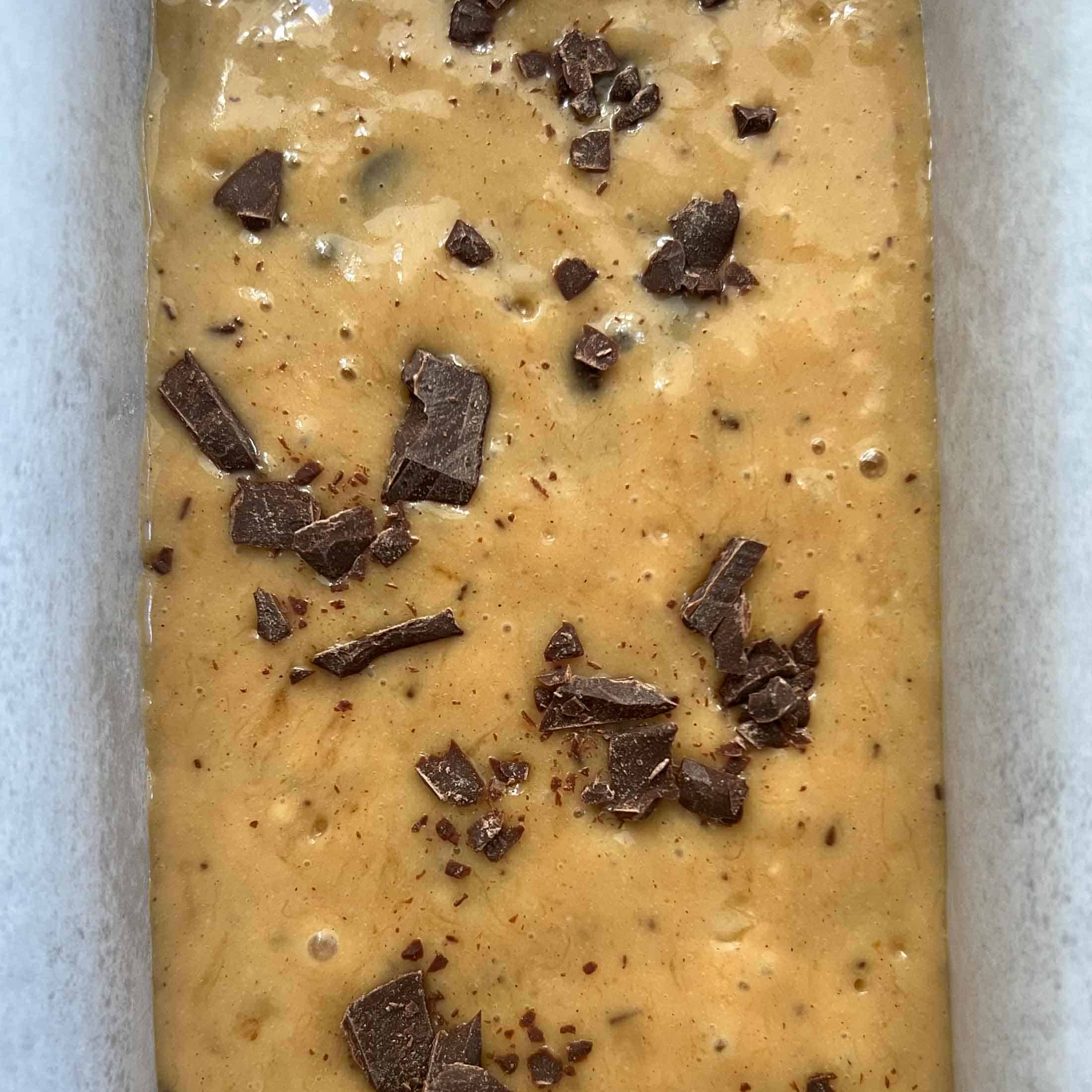 Chunks of chocolate sprinkled over a raw banana loaf.