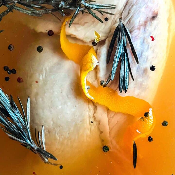 Turkey sitting under the brine with orange peels, rosemary, and peppercorns floating.