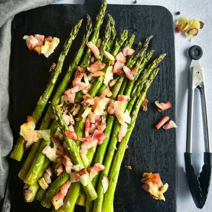 Traeger asparagus after being smoked, sprinkled with bacon, parmesan, mushrooms. Sitting on a black cutting board.