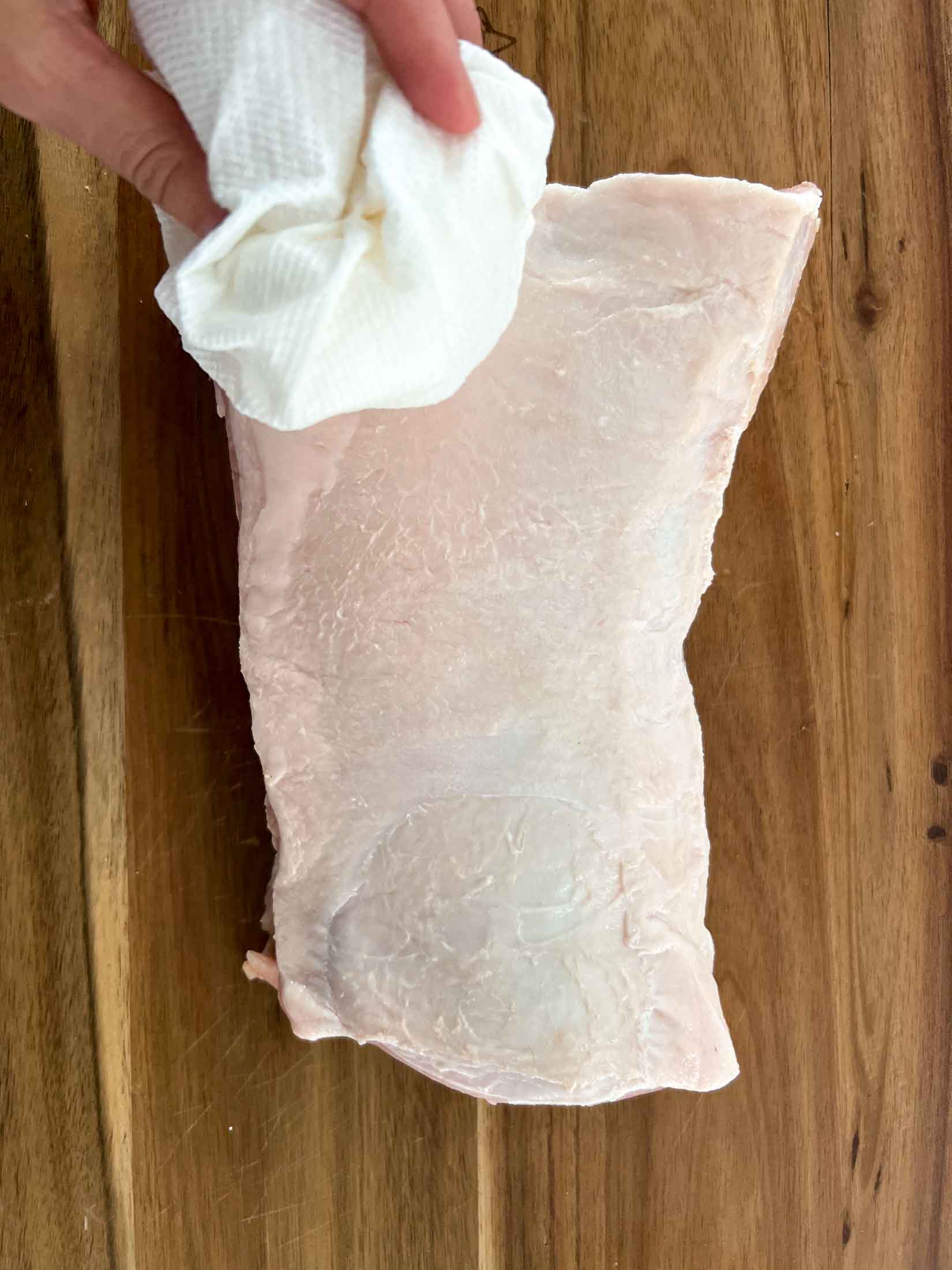 Paper towel patting a pork loin roast dry before smoking.