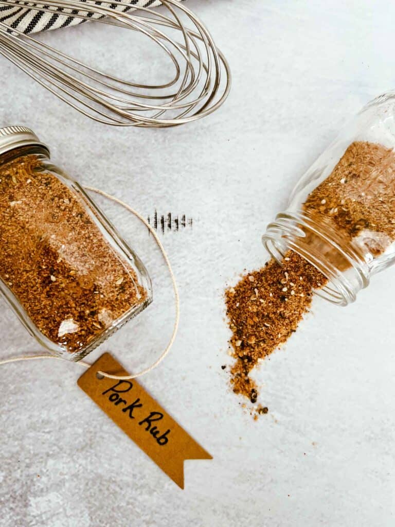 Pork rub in small glass spice jars. One spice jar is tipped over and the pork rub is spilling out.