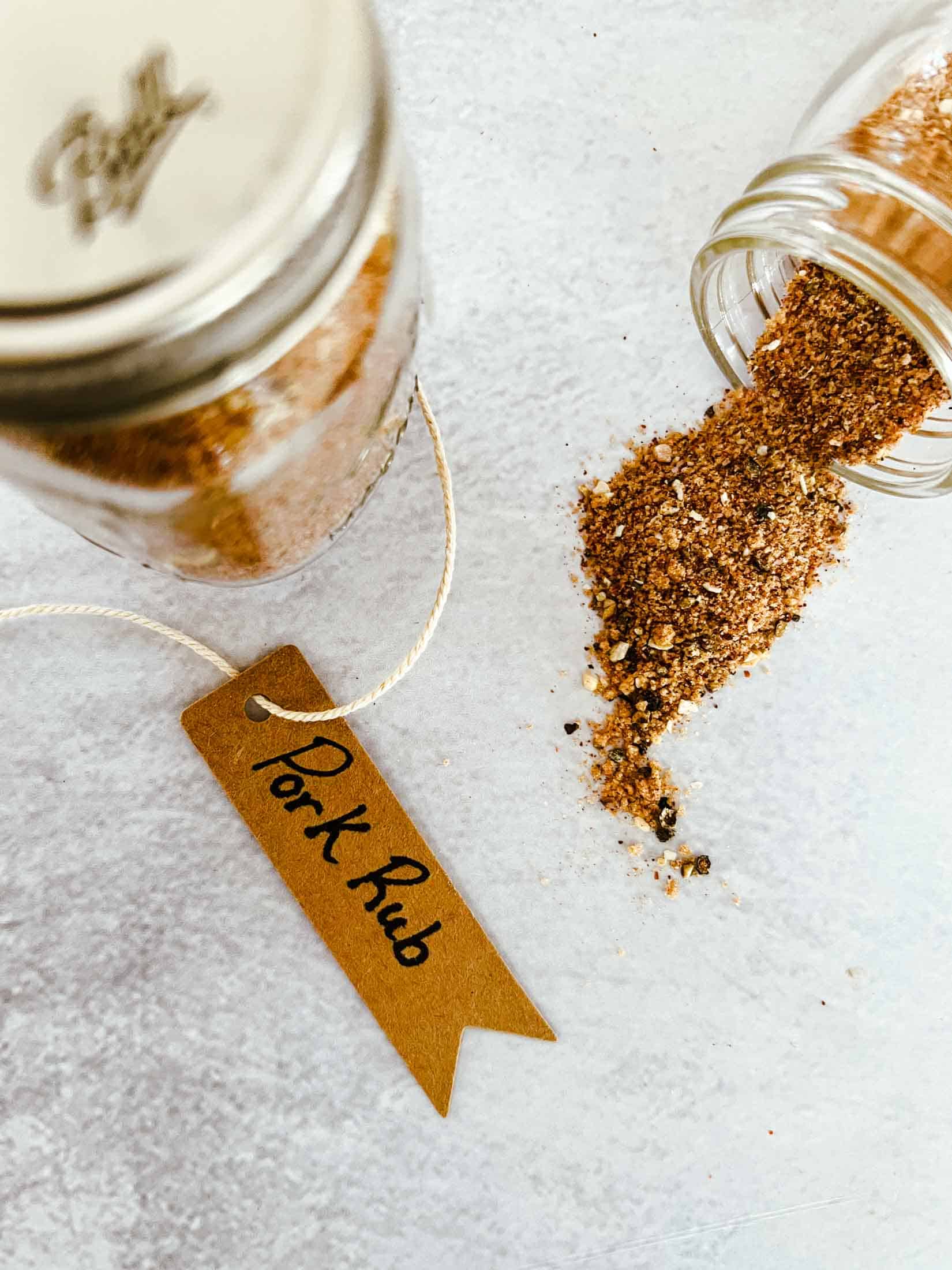 Pork rub in small glass spice jars. One spice jar is tipped over and the pork rub is spilling out.