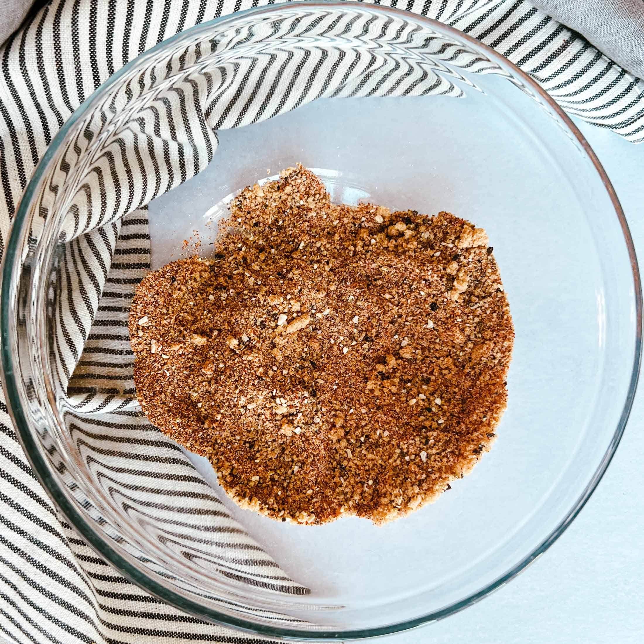 Spices and brown sugar loosely mixed in a glass bowl with a striped napkin in the background.
