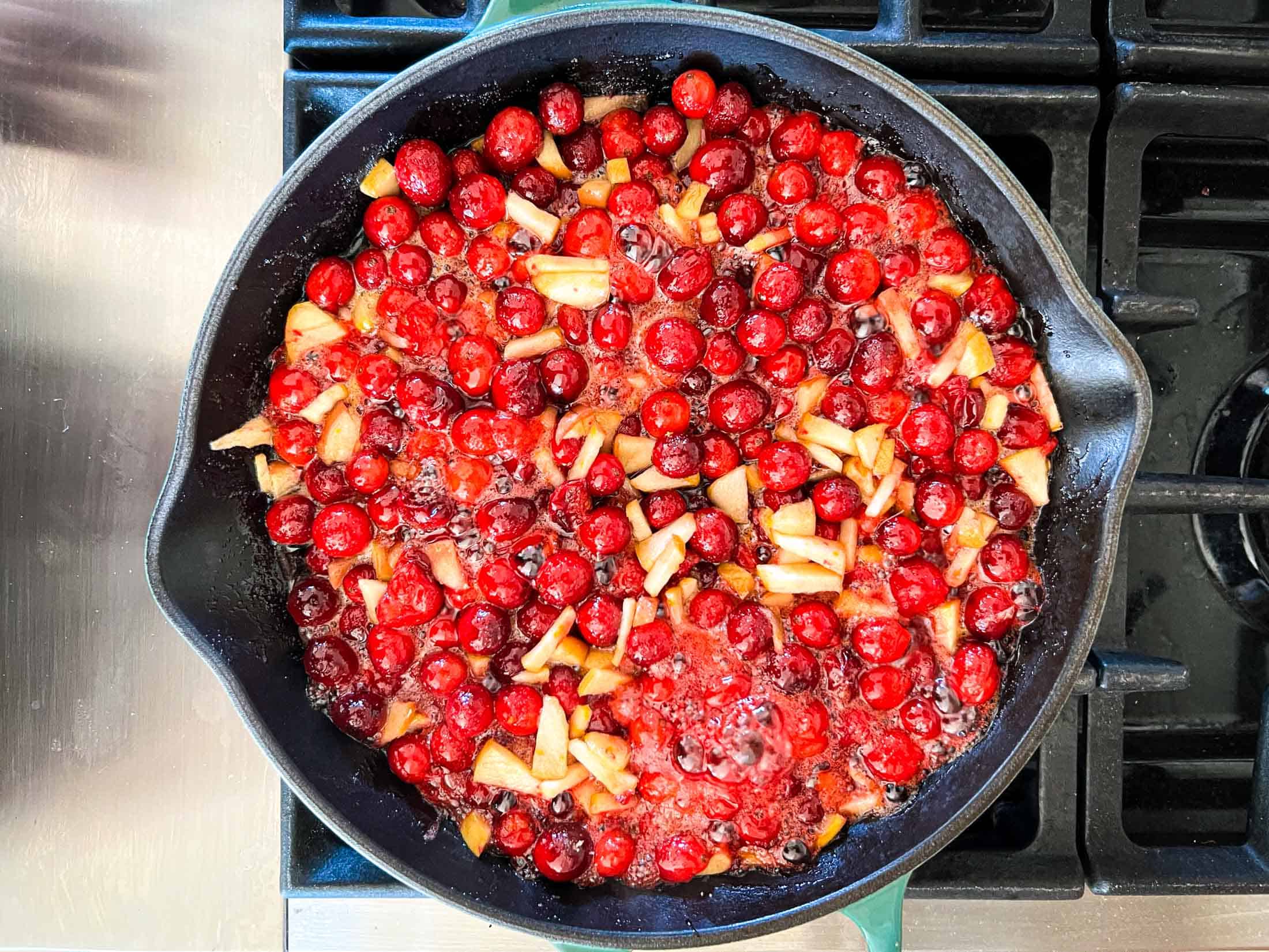 Cranberries, apples, and other ingredients boiling in a cast iron pan.