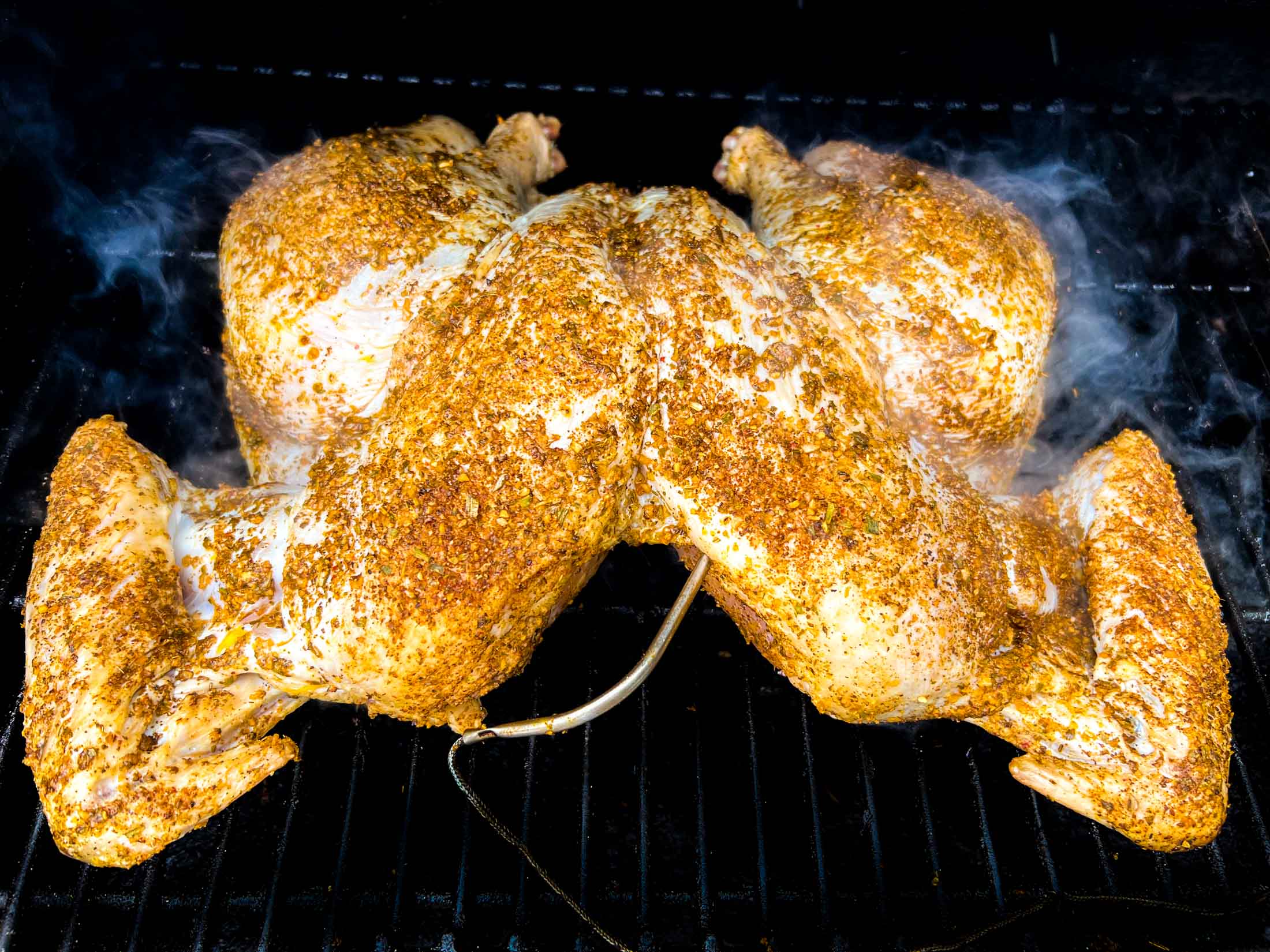 Spatchcock turkey on a pellet grill with smoke swirling around it.