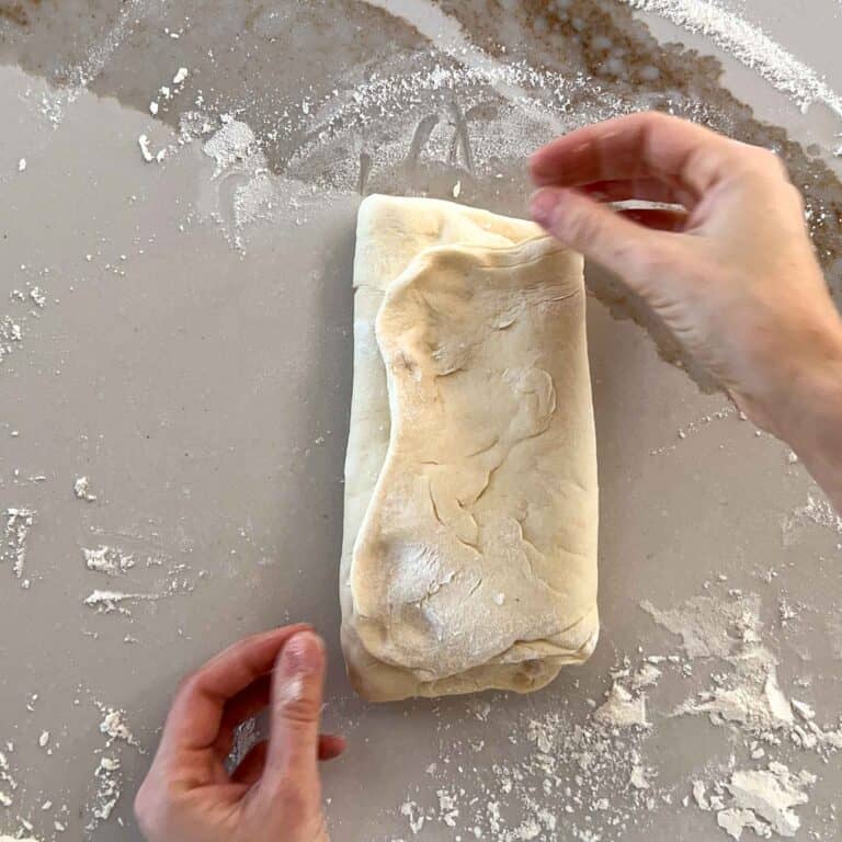 Shaping an uncooked loaf of sourdough sandwich loaf recipe.