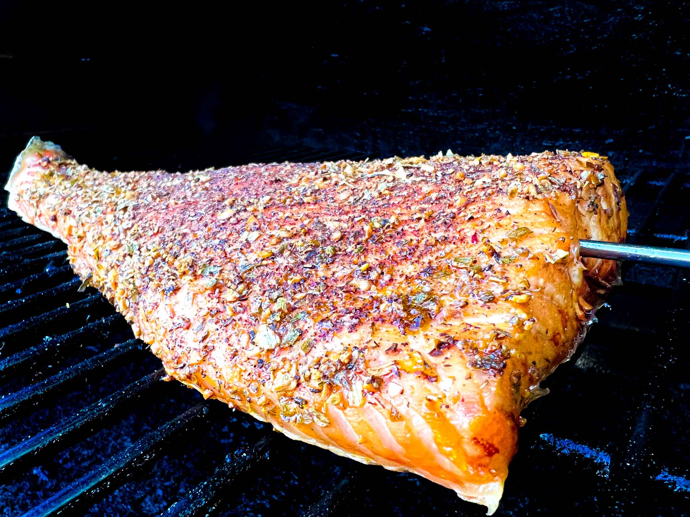 Large salmon fillet on a traeger pellet grill with a meat probe inserted.