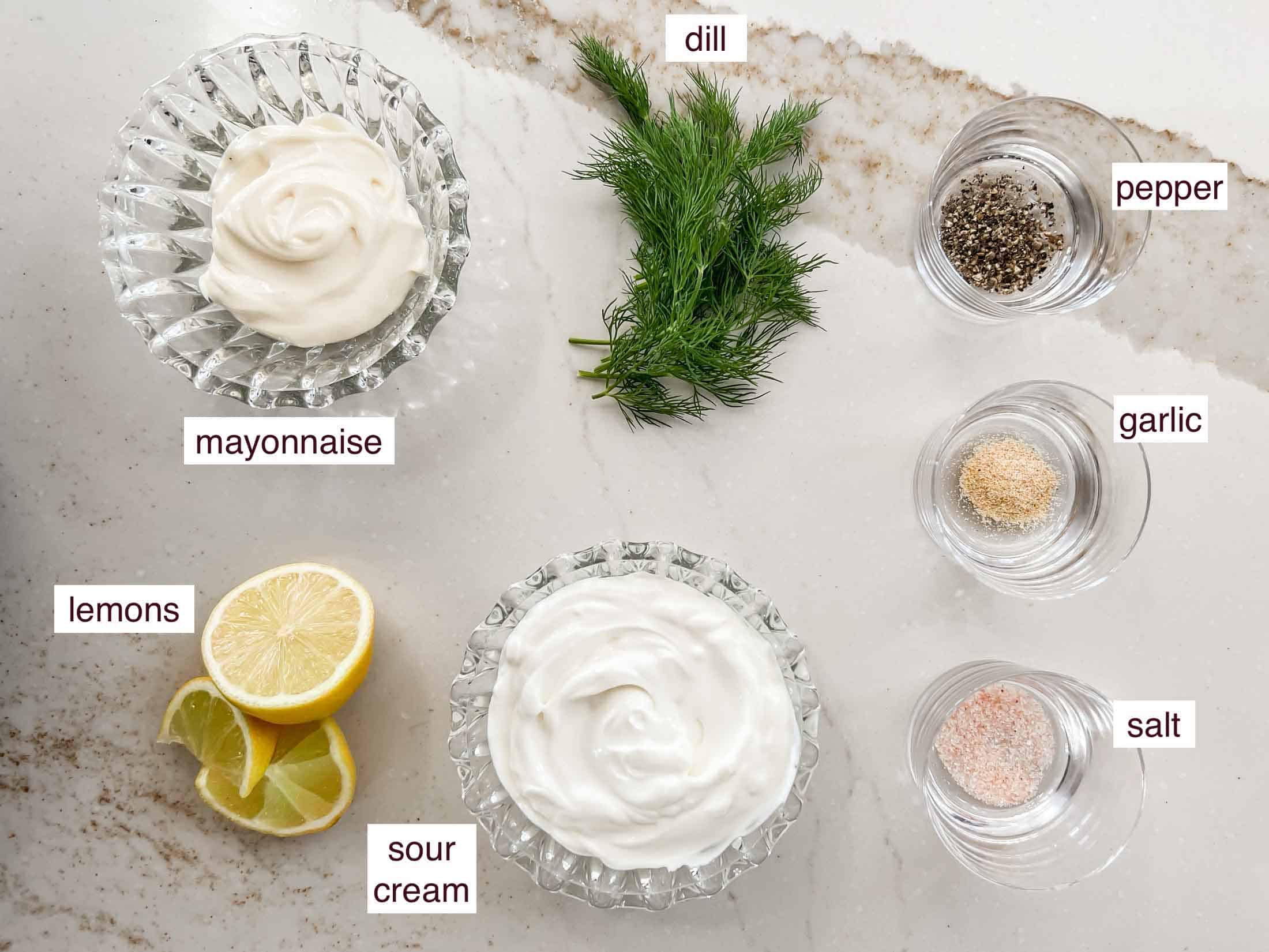 Key ingredients for creamy dill smoked salmon sauce including garlic, pepper, dill, mayo, lemons, sour cream, salt.