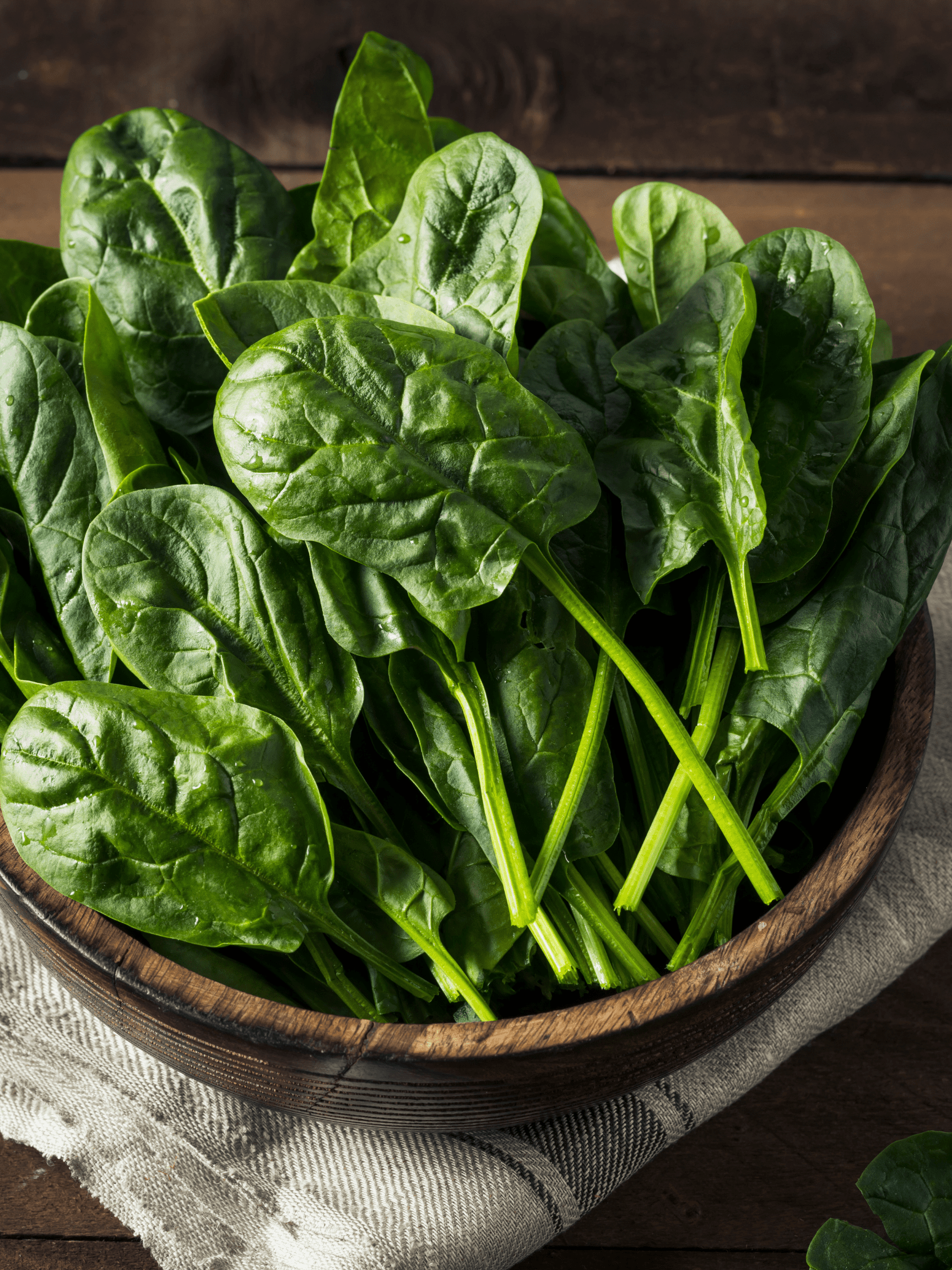 spinach in a wooden bowl on a white linen napkin