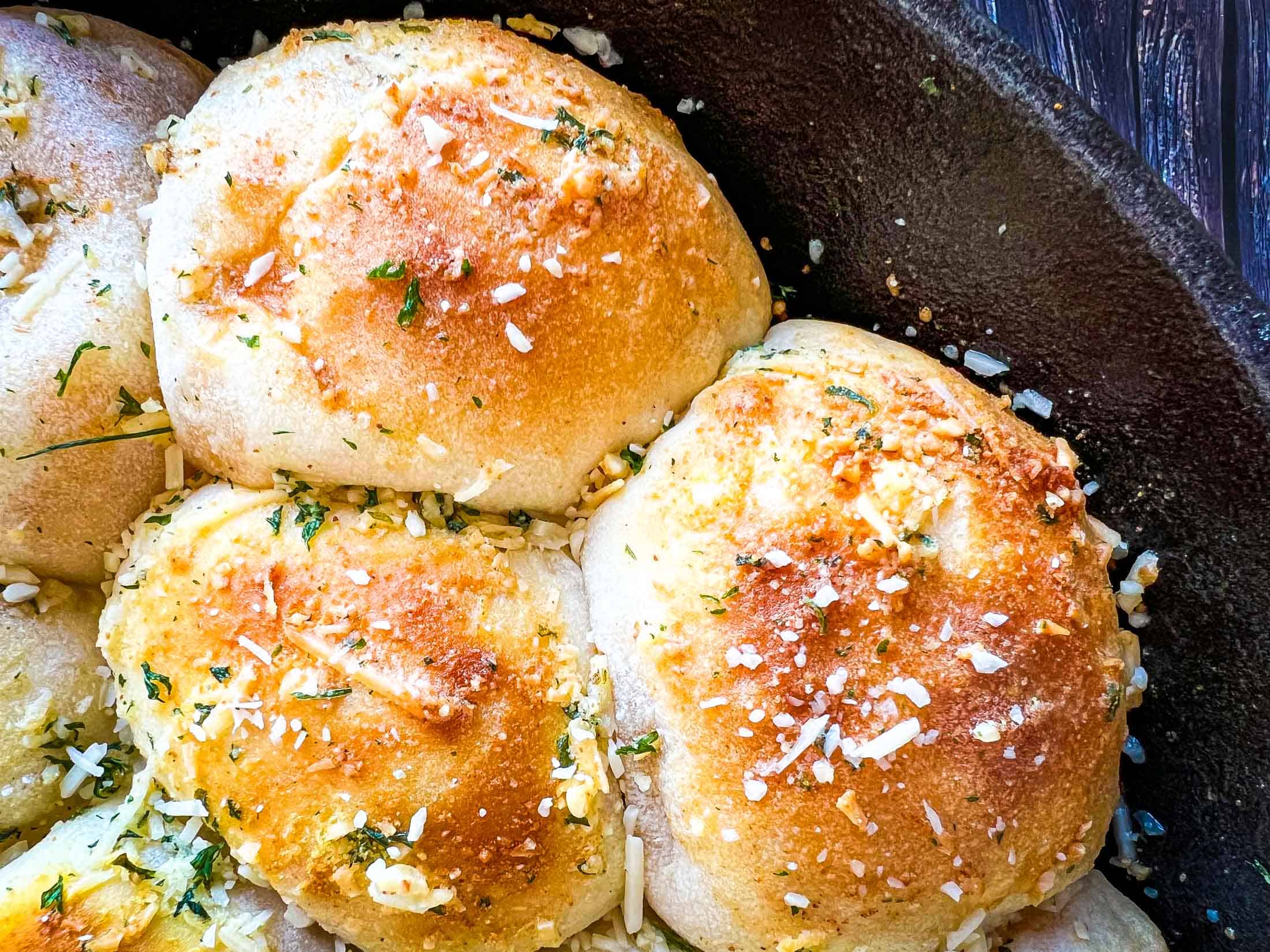 Close up picture of smoked buffalo chicken bombs in a cast iron pan with golden brown tops sprinkled with parmesan and parsley.