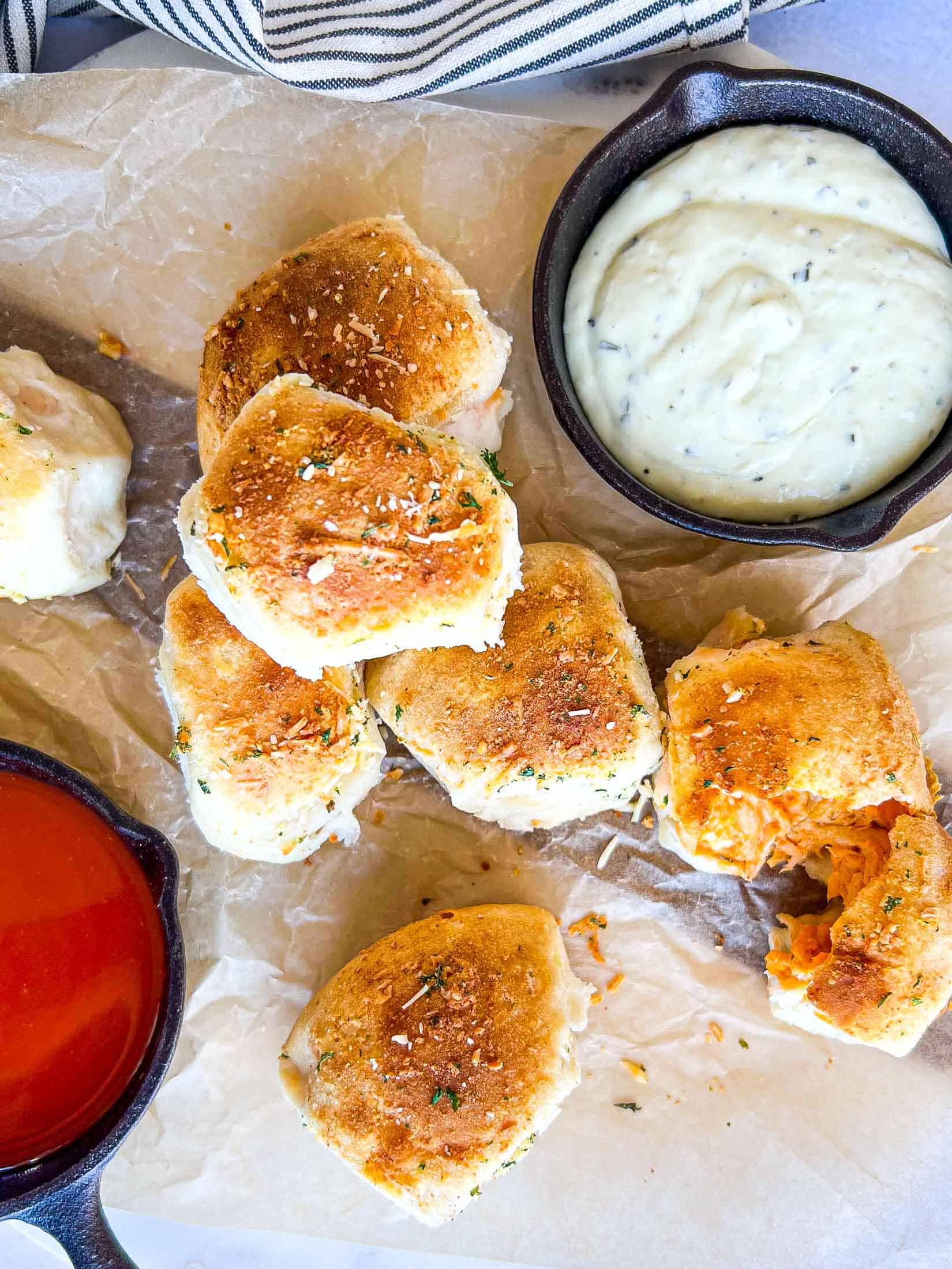 Buffalo chicken bombs piled on top of each other with one torn open and ranch and buffalo dipping sauce on the side.