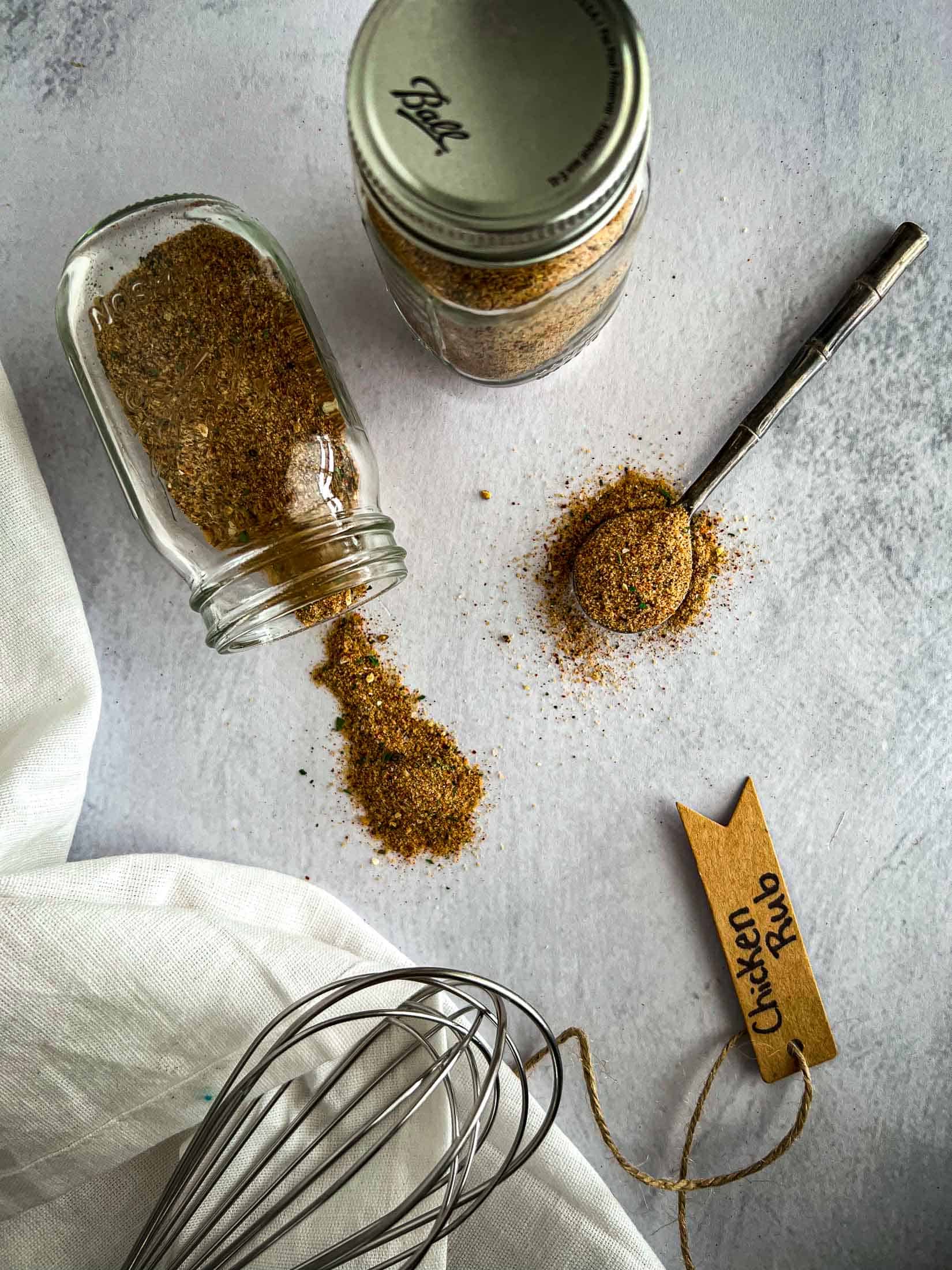 Smoked chicken rub spilling out of a spice jar with a metal spoon full of rub.