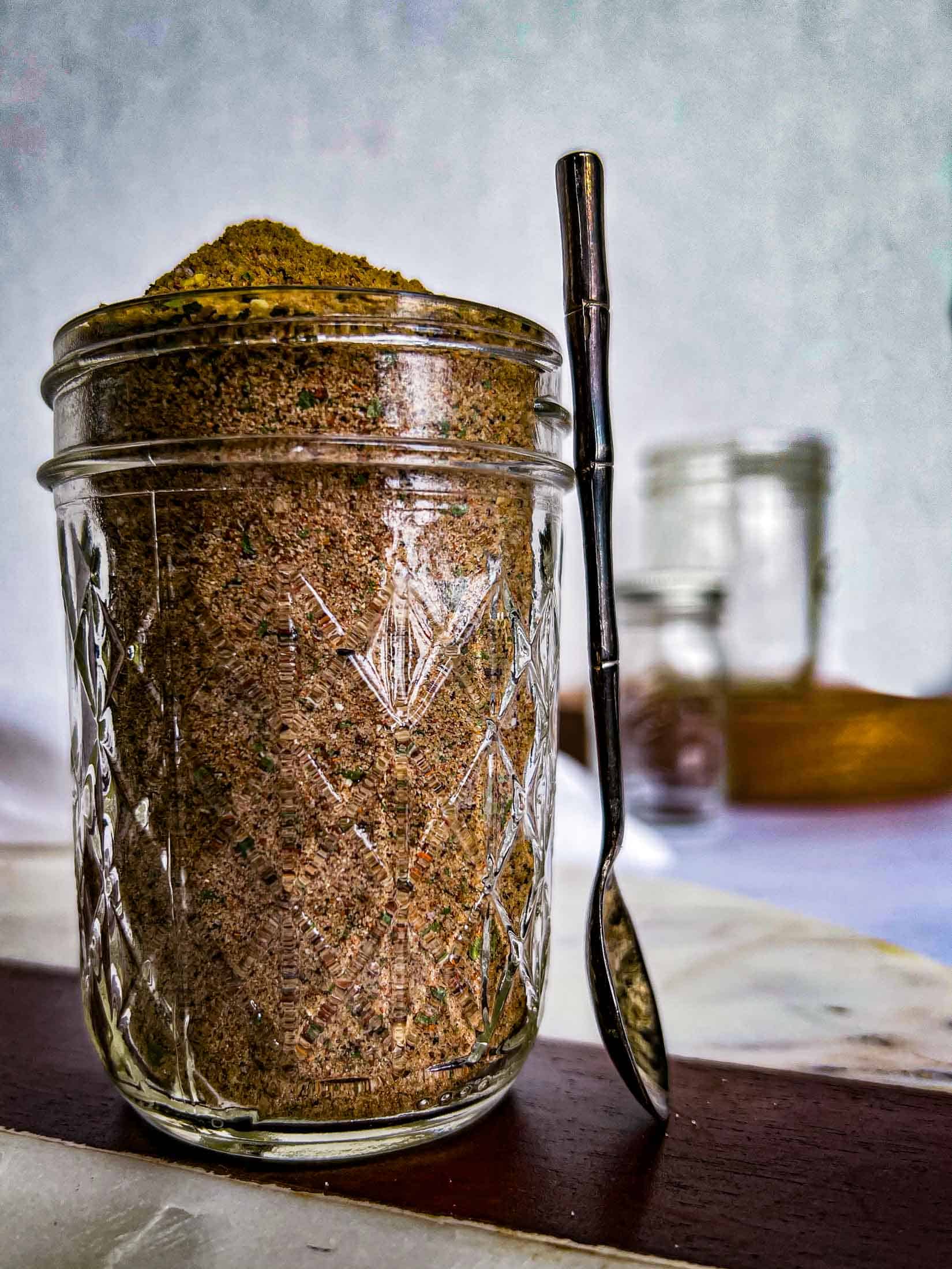 A heaping quarter pint of smoked chicken rub with a metal spoon resting on the jar.