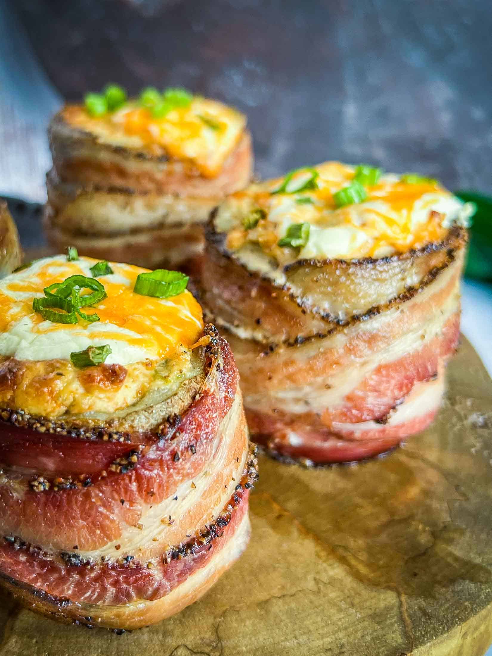 Close up view of bacon wrapped smoked volcano potatoes showing peppered bacon, sour cream, and fresh chives.