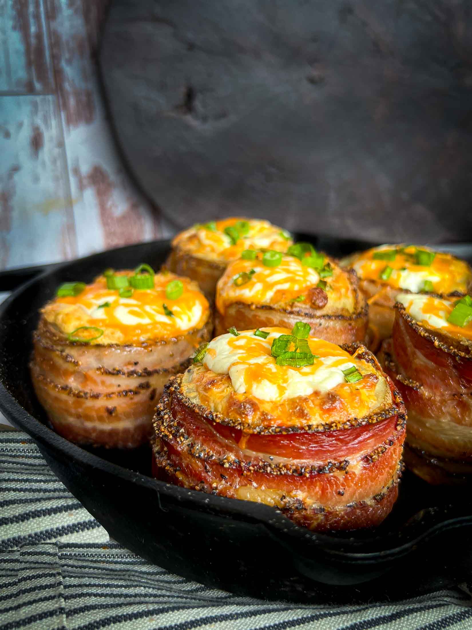 Bacon wrapped volcano potatoes in a cast iron pan with chives, sour cream, and cheese on top.