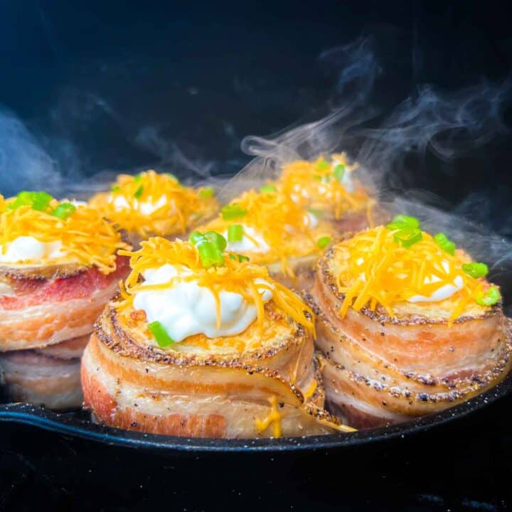 Smoky baked potatoes with volcano filling, wrapped in bacon and sitting in a cast iron pan on a pellet grill.
