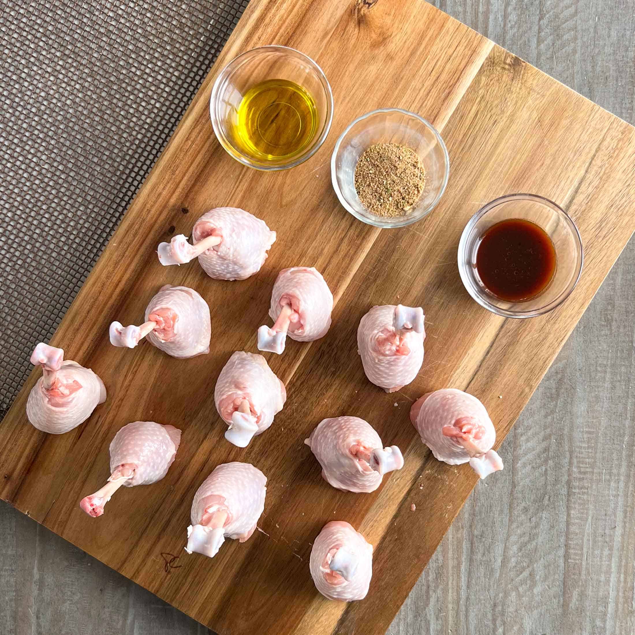Eleven frenched drumsticks ready to be seasoned with olive oil, rub, and barbecue sauce in bowls.