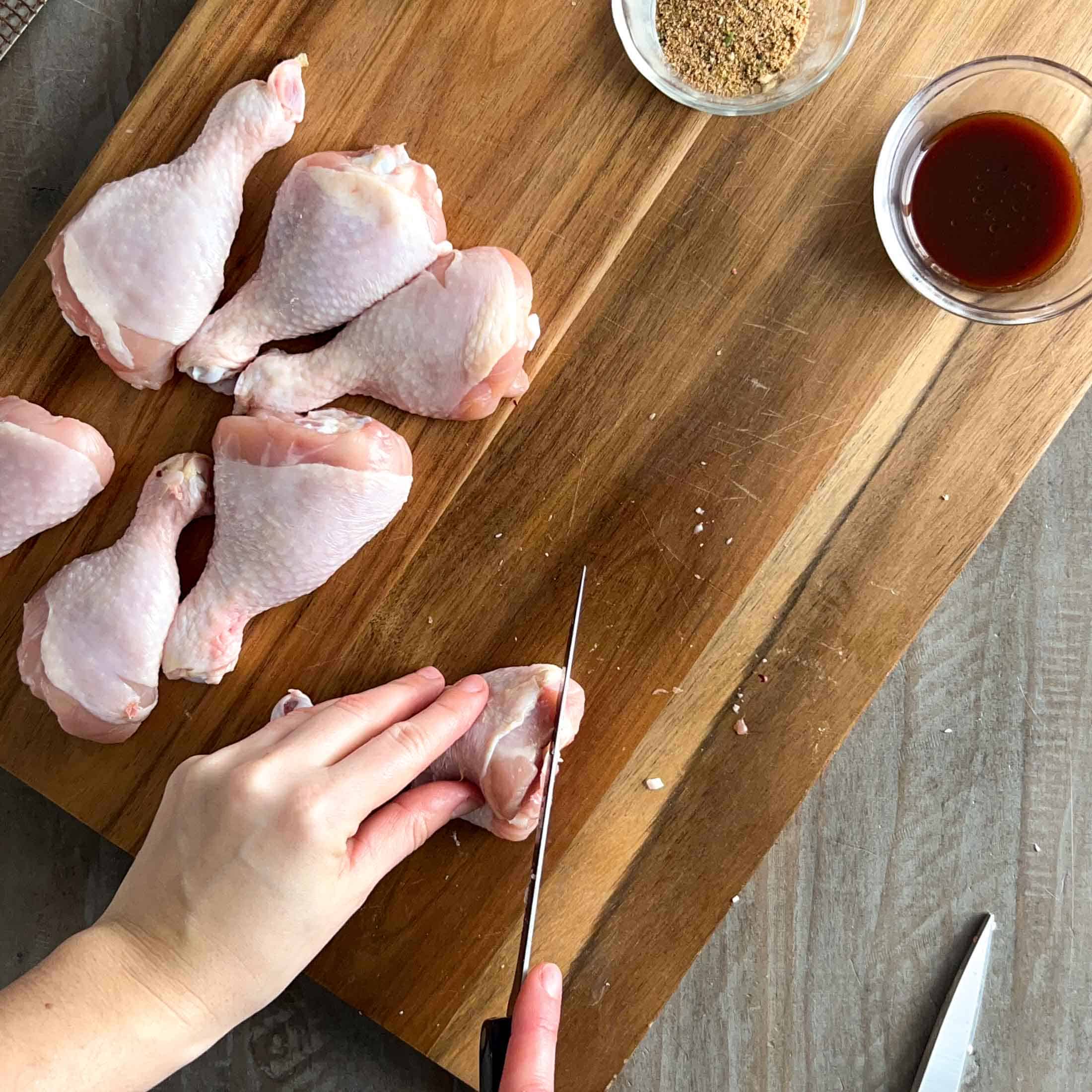 A sharp knife cutting the bottom off of a chicken drumstick to help it stand straight.
