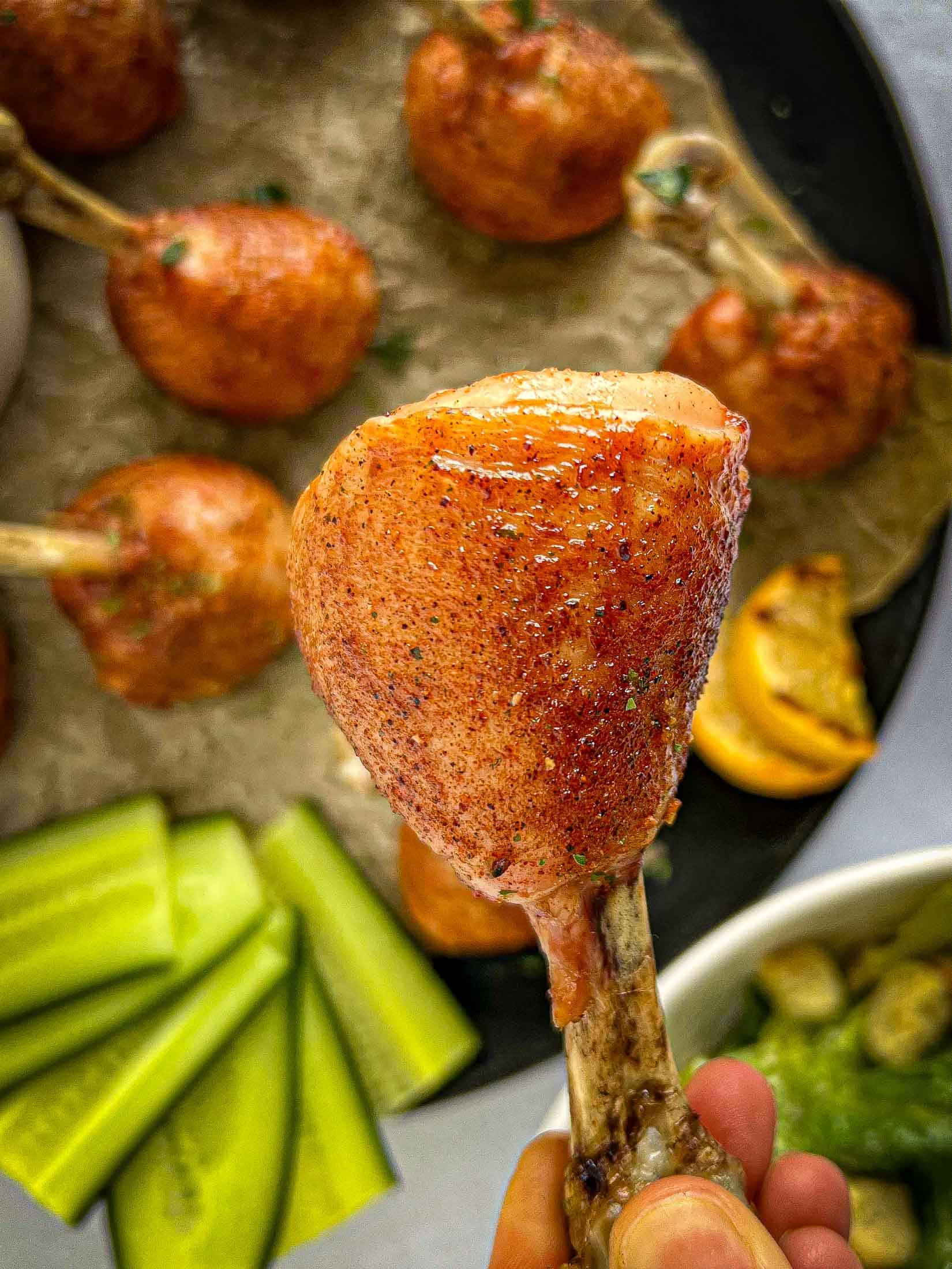 A grilled chicken lollipop drumstick being held out to showcase the finished product.