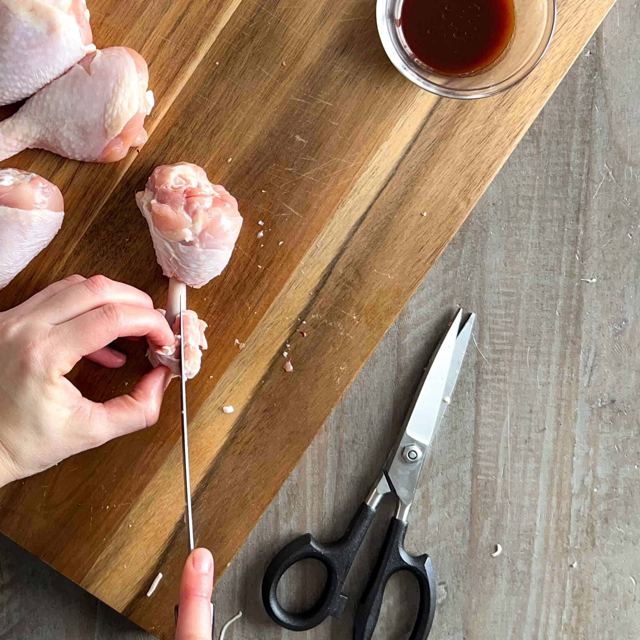 The top skin on a chicken drumstick being cut away to make a chicken lollipop.