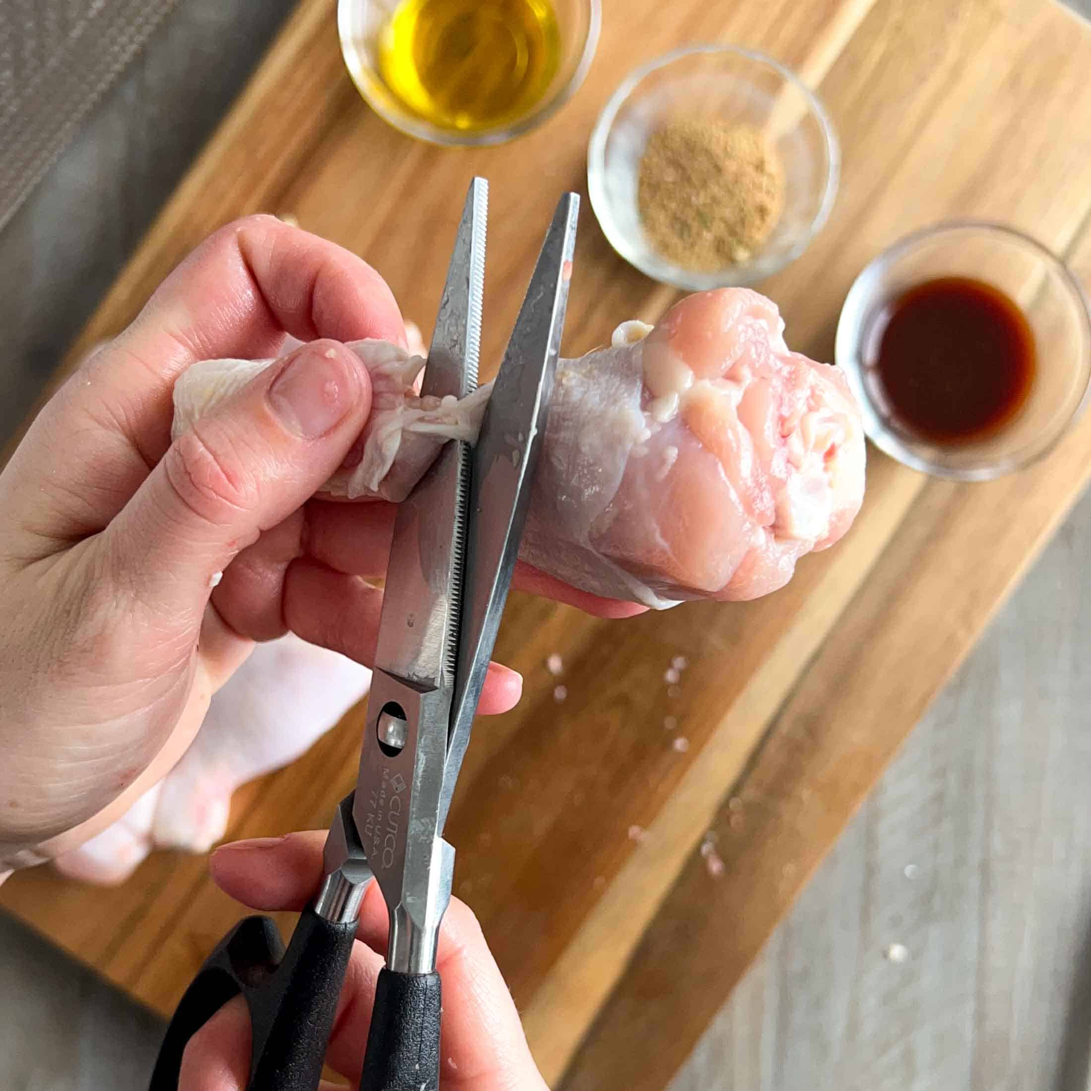 Kitchen shears cutting through extra skin and tendons on a chicken lollipop.