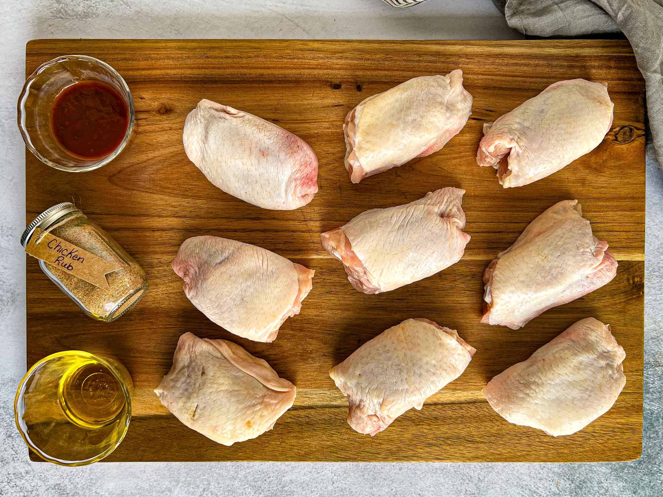 Key ingredients for smoked chicken thighs including chicken rub, barbecue sauce, and olive oil.