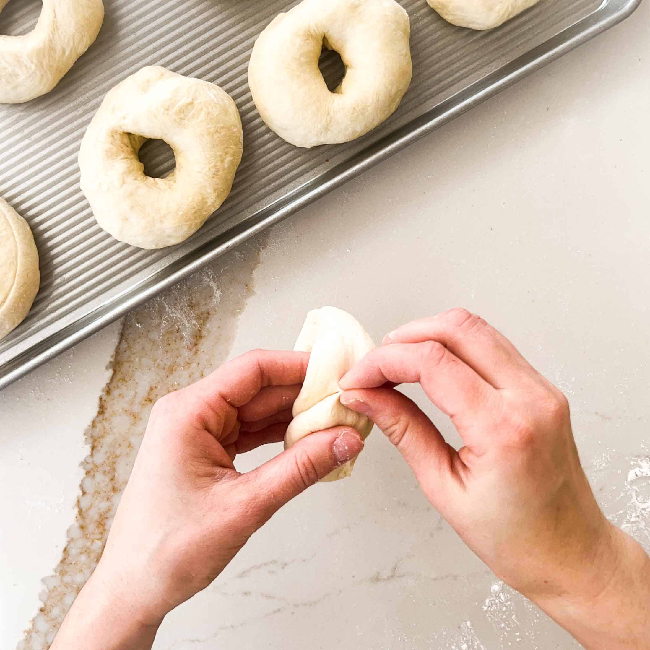 Joining dough at the ends and pinching to form a bagel.