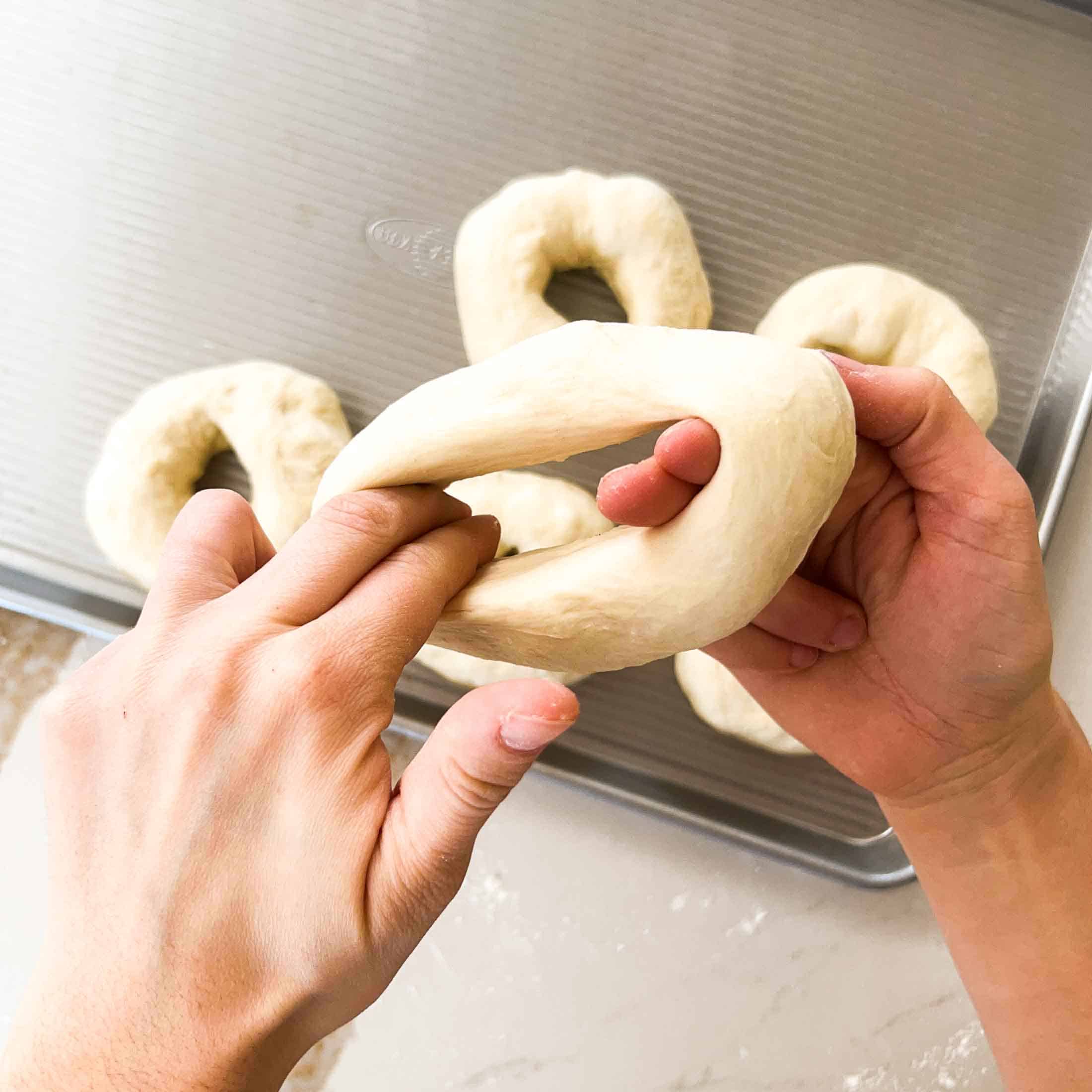 Gently stretching bagel dough to form holes in the middle.