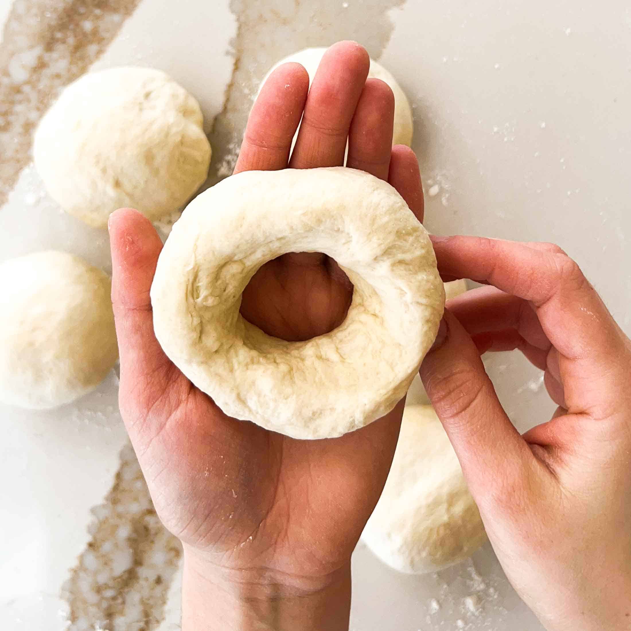 Fully formed raw bagel in the palm of a hand.