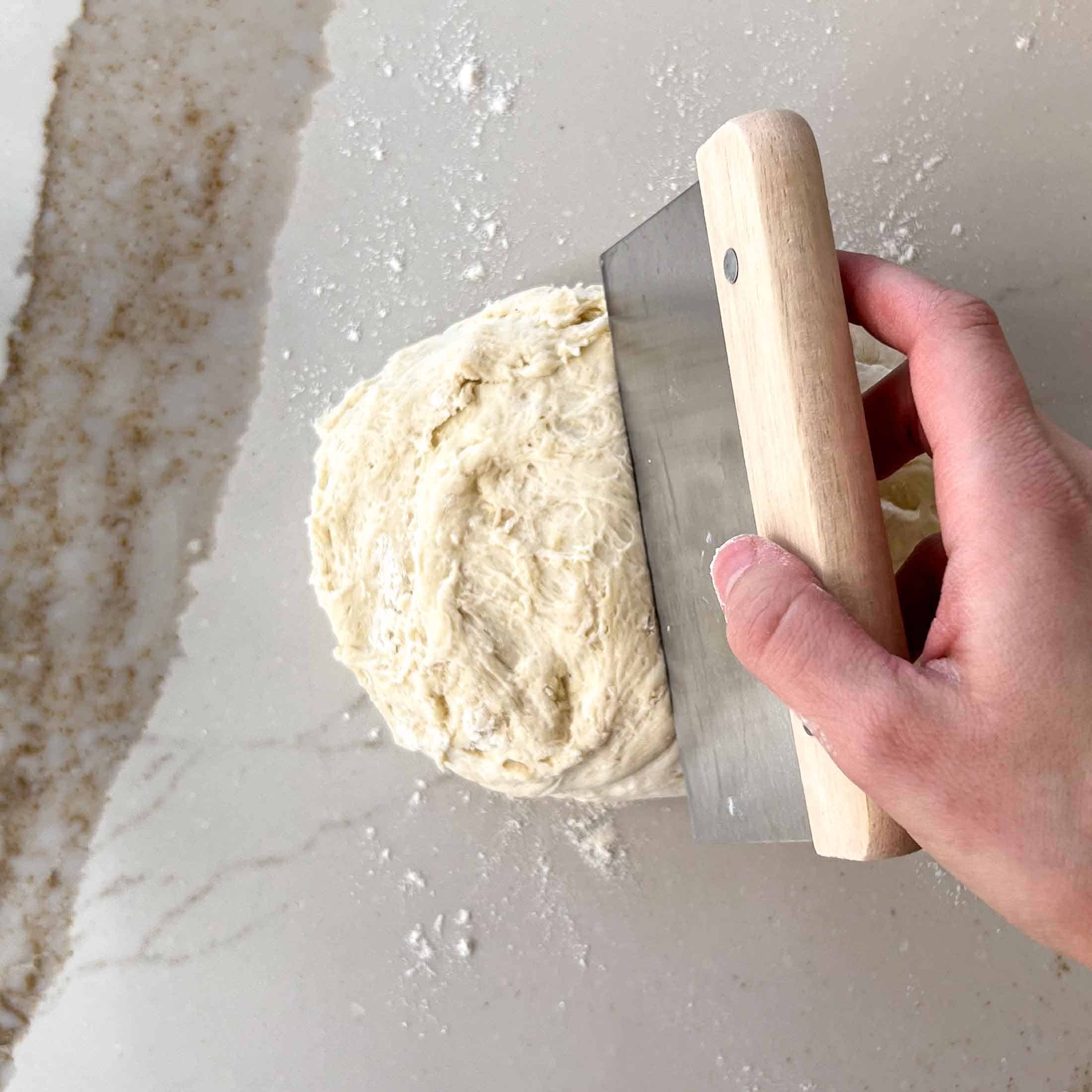 A bench scraper cutting into a ball of dough.