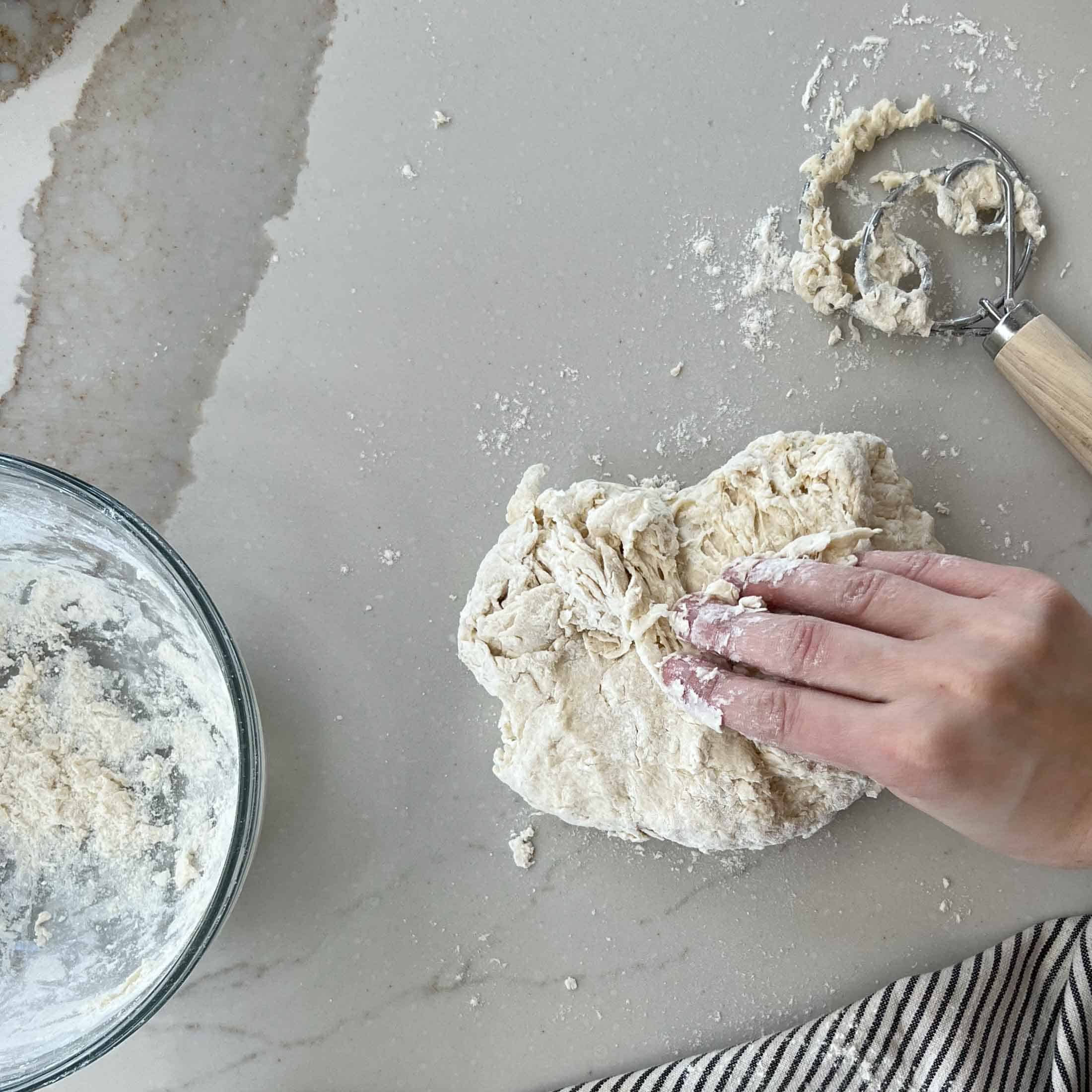 Shaggy naan dough being kneaded on a floured work surface.
