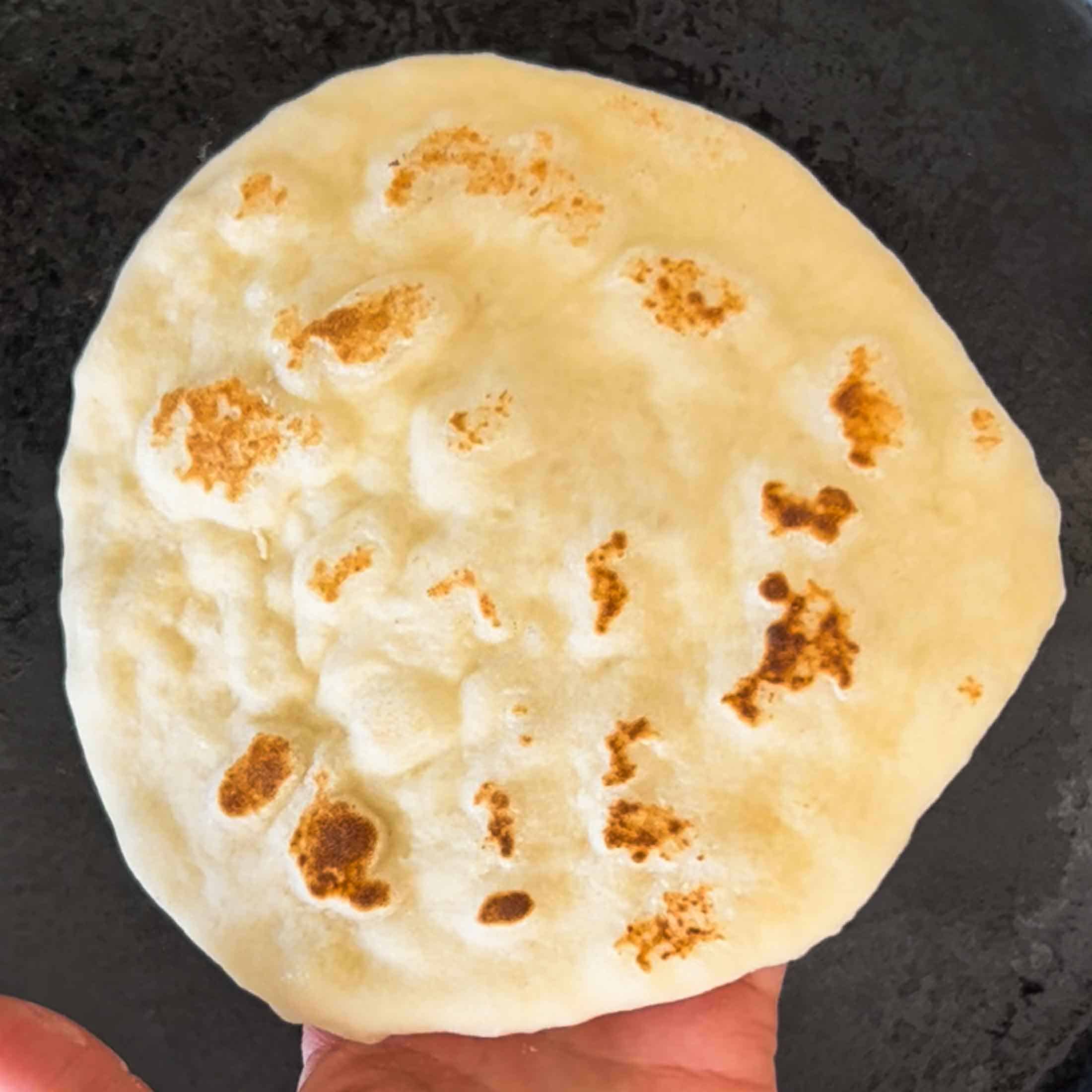 The underside of a freshly cooked sourdough discard naan bread showing golden brown bubbles.