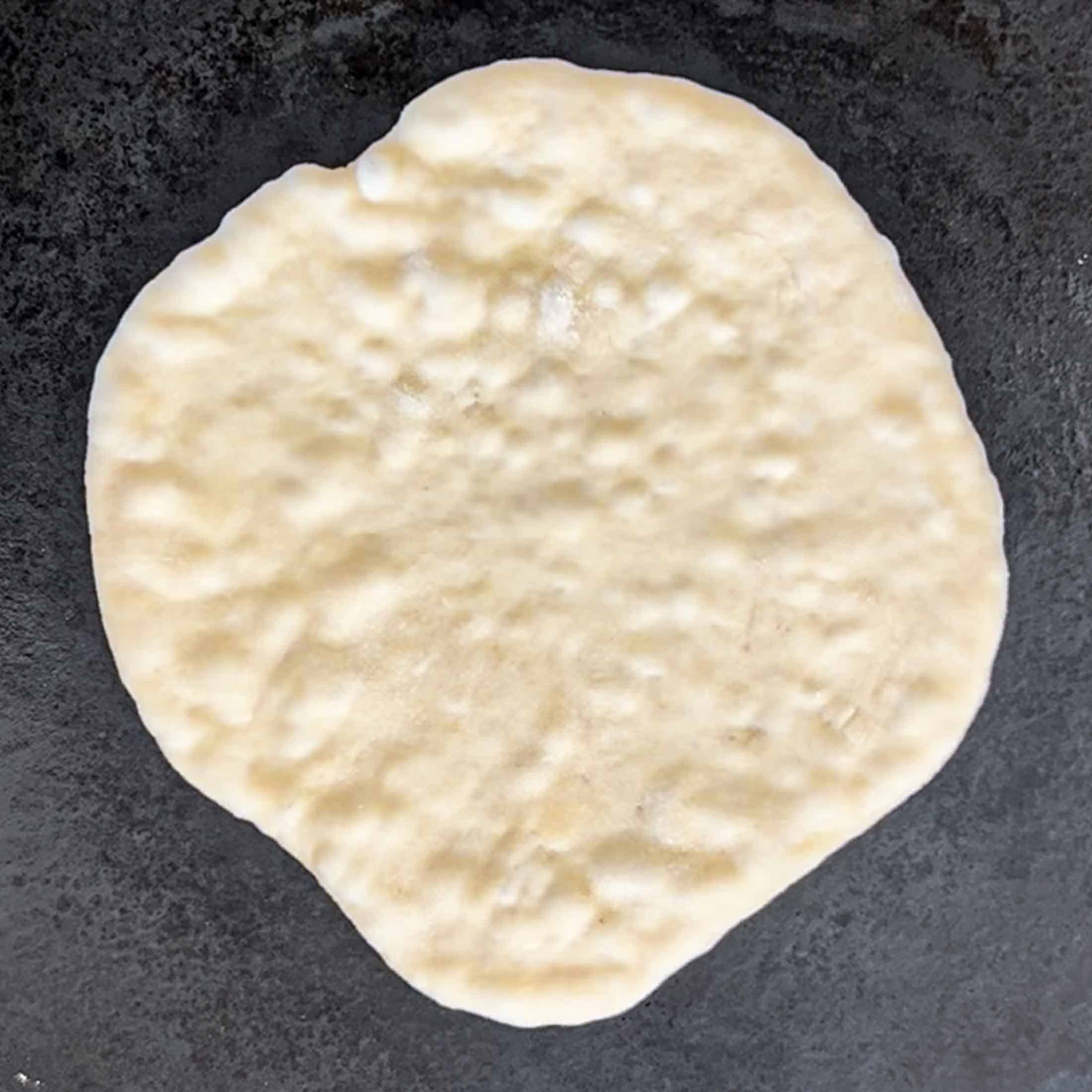Sourdough naan bread on a hot cast iron pan, starting to bubble.