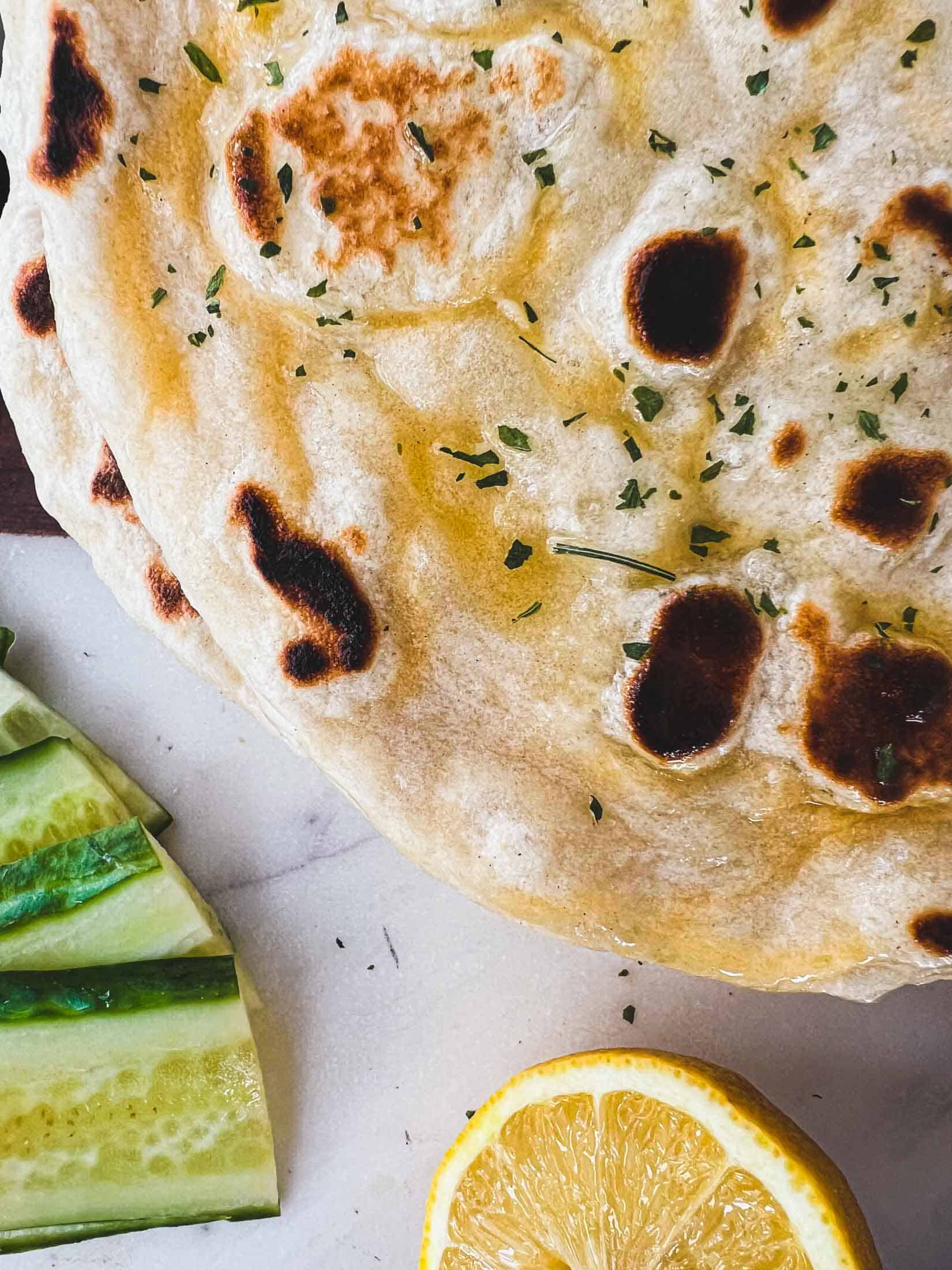 Closeup picture of naan bread with olive oil and parsley overtop.