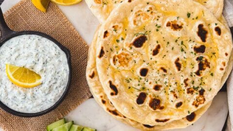 Sourdough naan bread piled up with lemons, cucumbers, and taztziki.