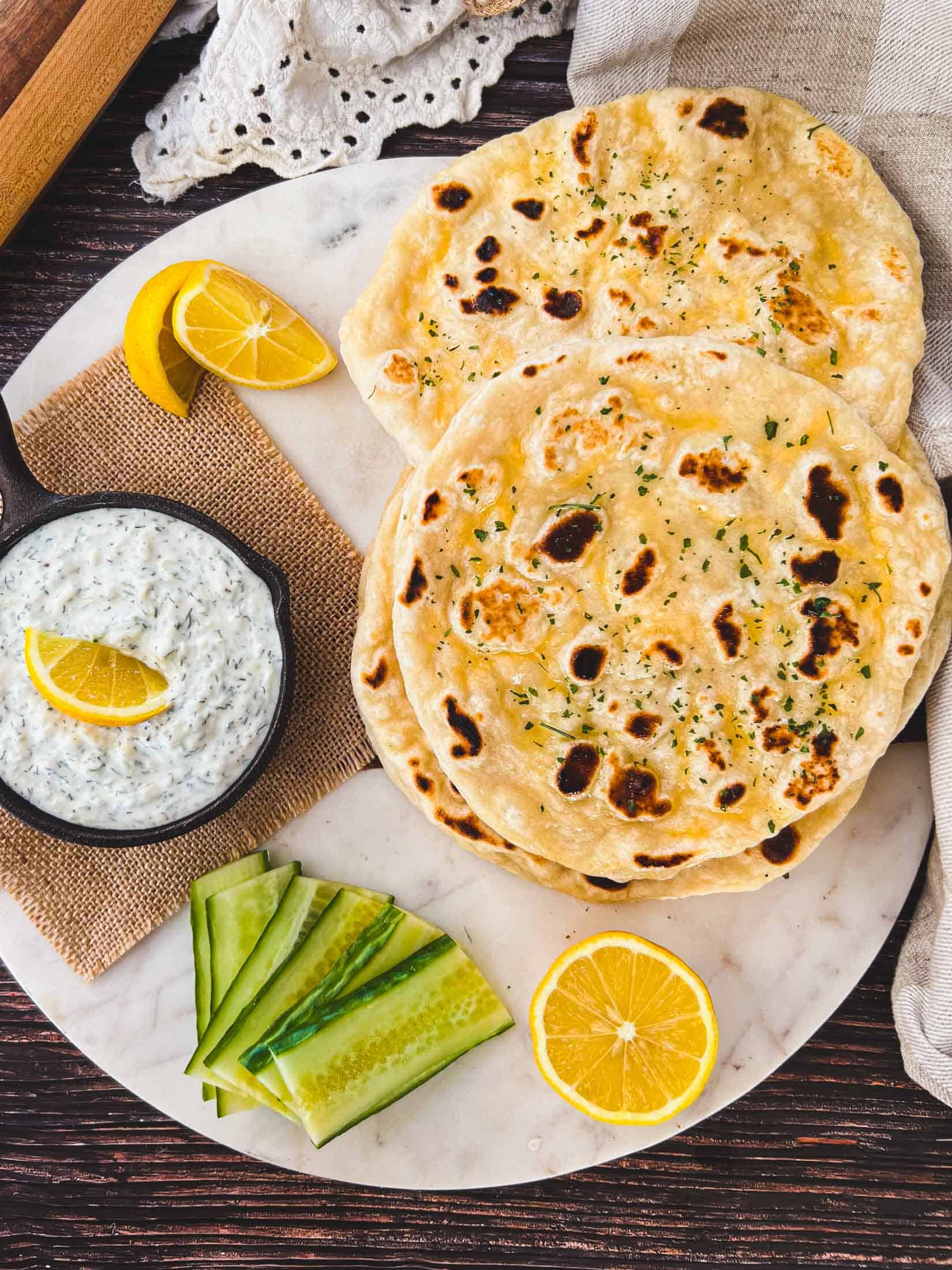 Sourdough naan bread piled up with lemons, cucumbers, and taztziki.