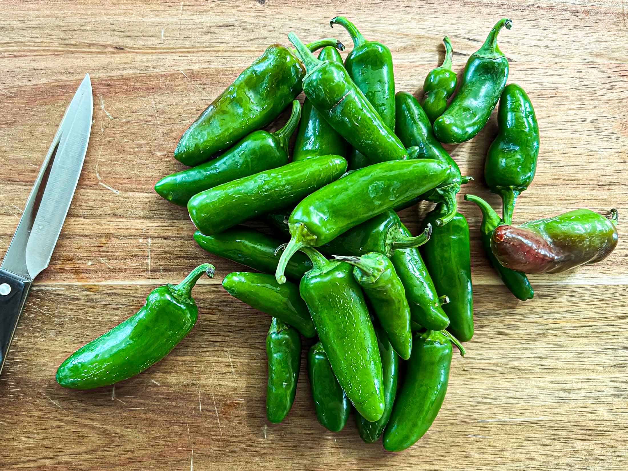 Jalapeno peppers on a wooden cutting board with a sharp knife.