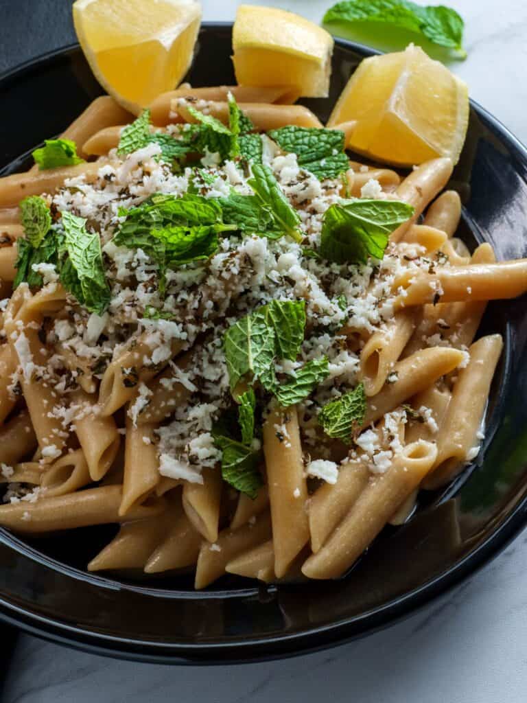 Pasta with mint, mushrooms and parmesan on a black stone plate.