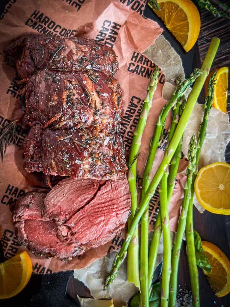 smoked venison tenderloin on butcher paper with asparagus and oranges all around.
