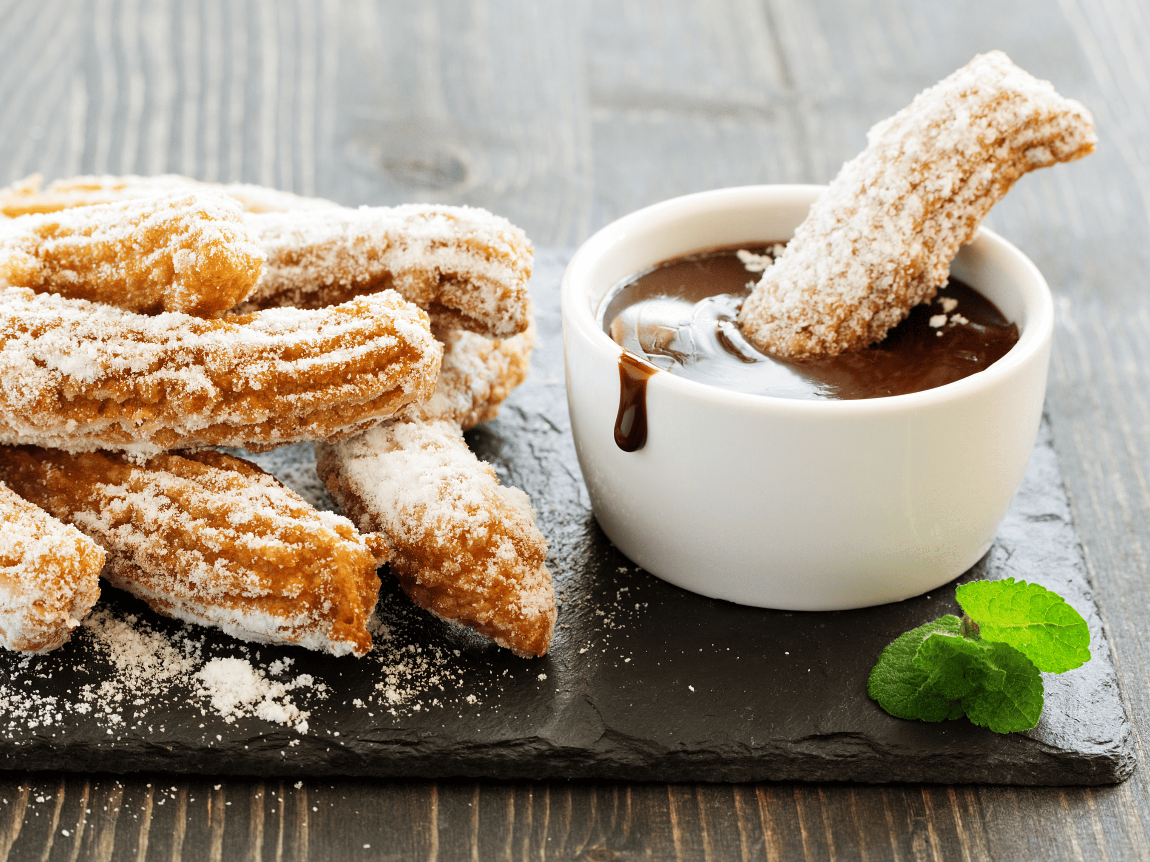 Fresh churros being dipped in chocolate sauce.
