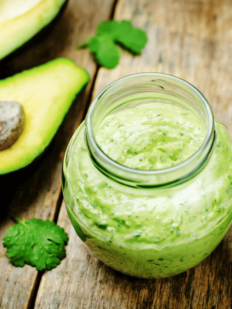 Cliantro lime dressing with avocado in a glass jar on a wooden surface. 