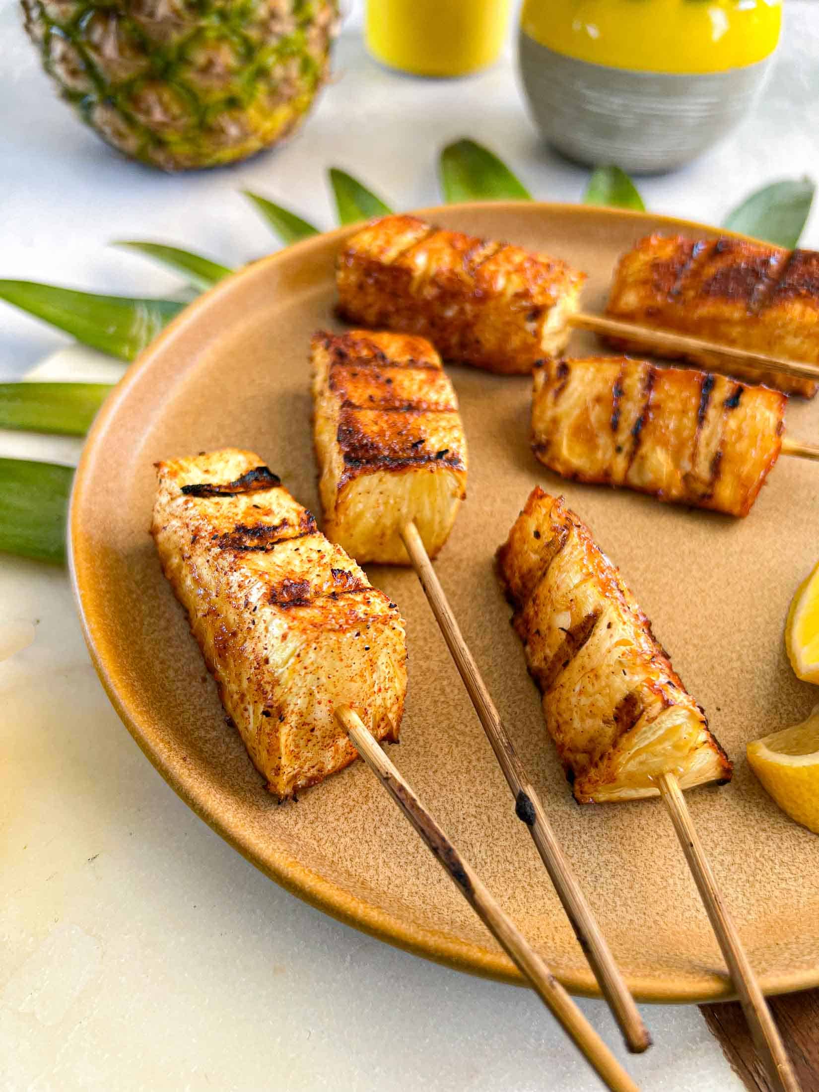Grill marks on smoked pineapple skewers with pineapple leaves and lemon.